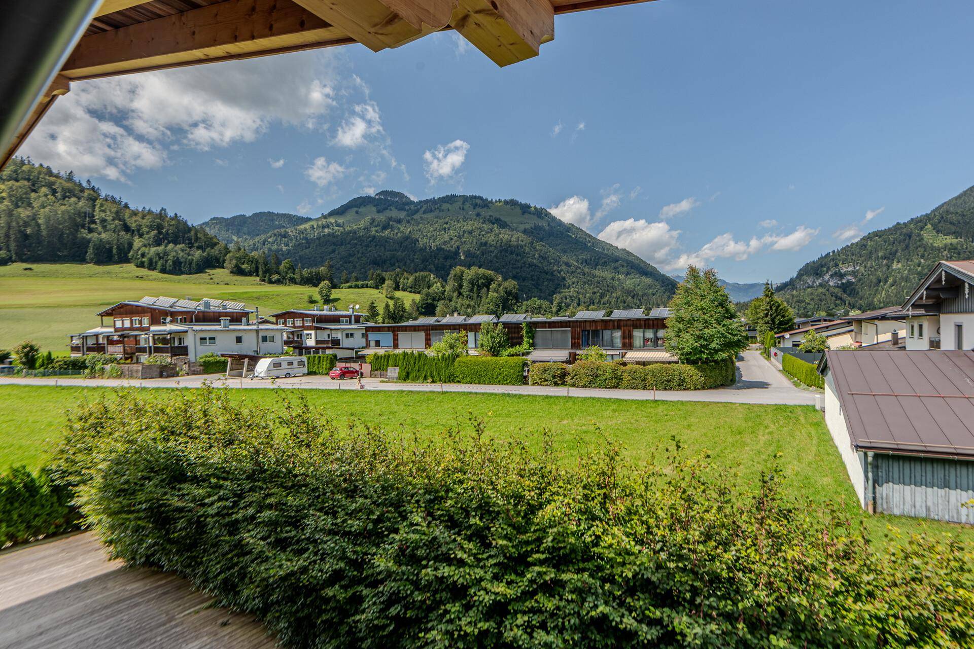 Weitläufiger Blick über die grüne Landschaft und die Dächer der Häuser bis zu den majestätischen Bergen.