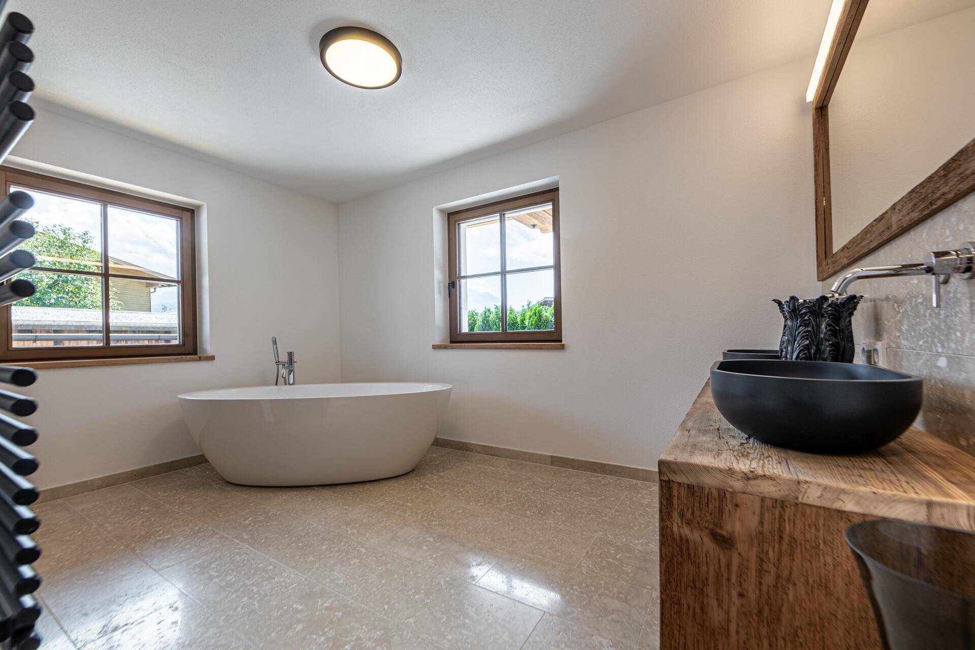 Geräumiges Badezimmer mit freistehender Badewanne, Doppelwaschbecken und Holzwaschtisch unter zwei Fenstern.