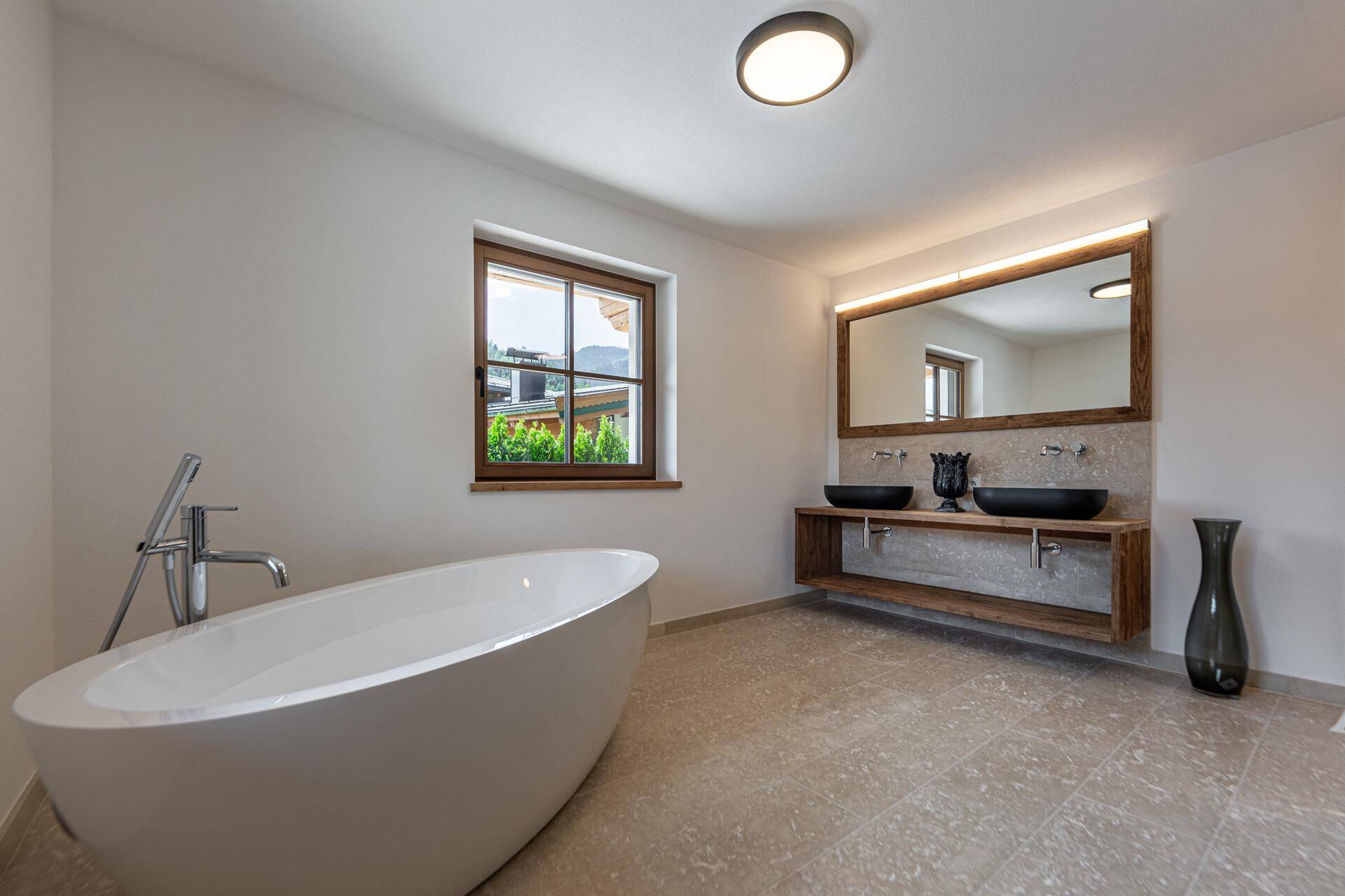 Helles Badezimmer mit freistehender Badewanne, Doppelwaschbecken und großem Spiegel mit Holzrahmen.
