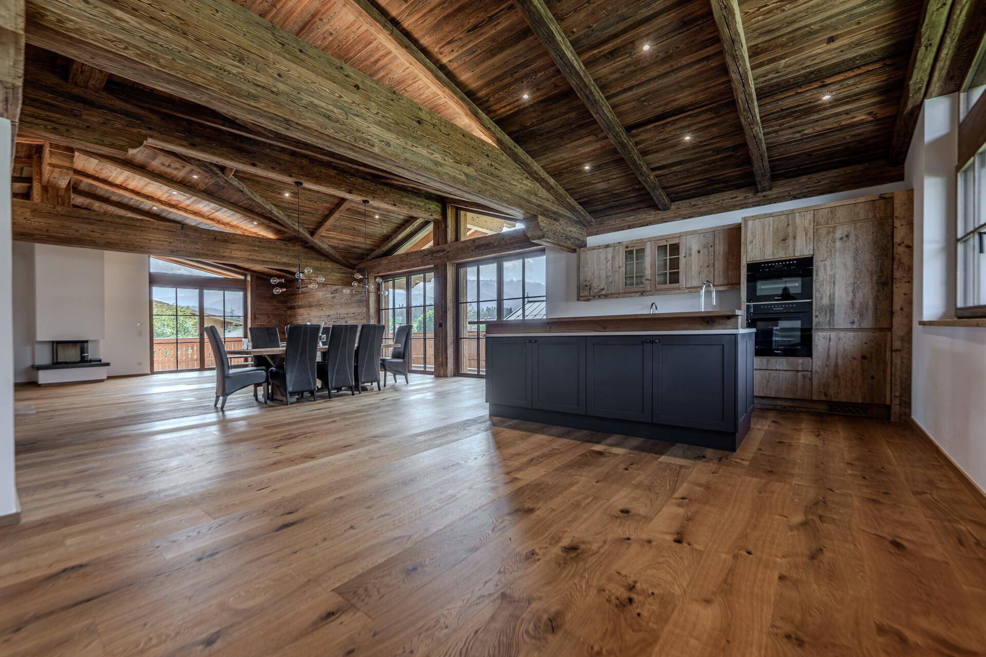 Offene Wohnküche mit Kücheninsel, Essbereich und Wohnzimmer, alles unter einer beeindruckenden Holzbalkendecke.