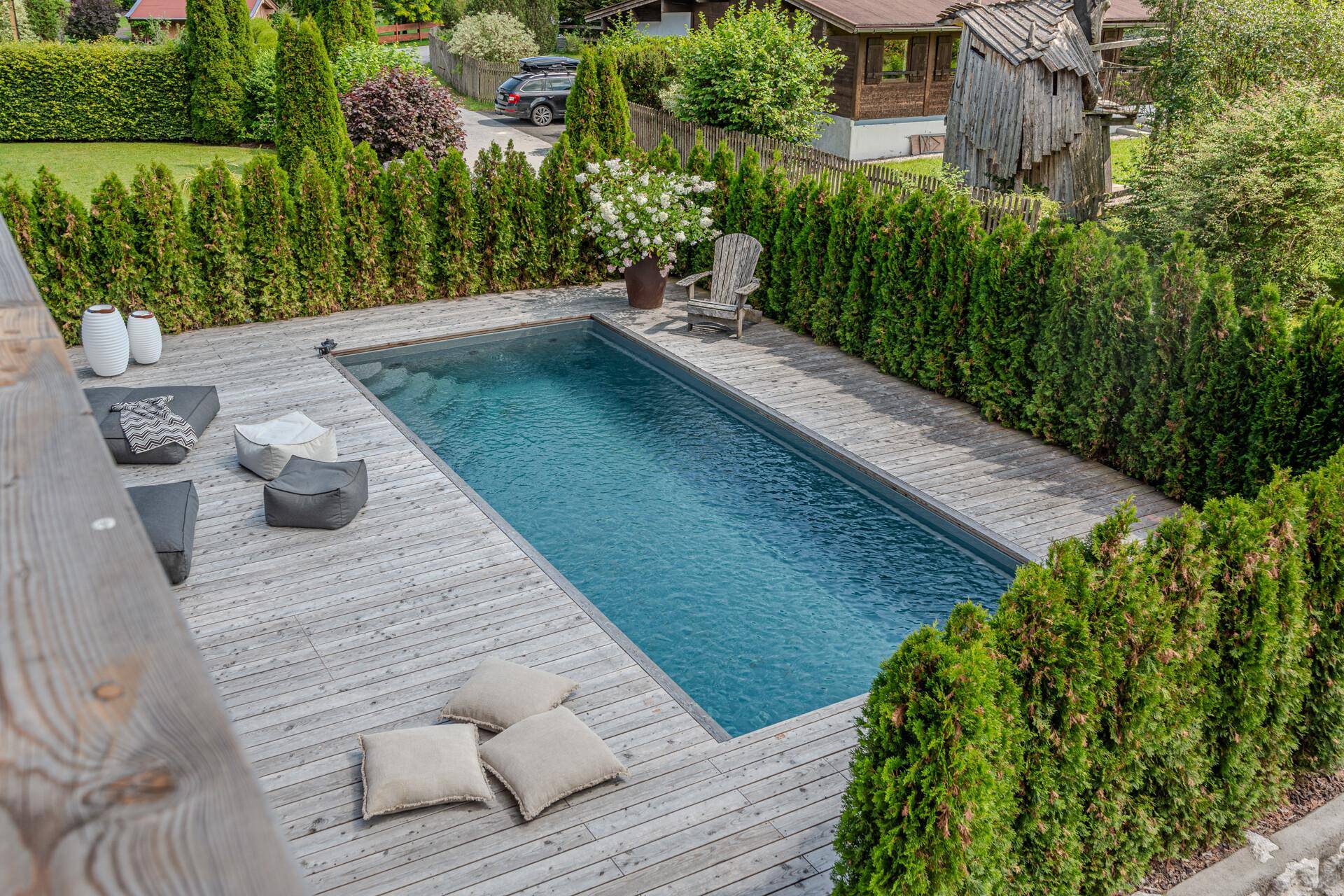 Rechteckige Poolanlage mit umlaufendem Holzdeck und einer dichten grünen Hecke für Privatsphäre.