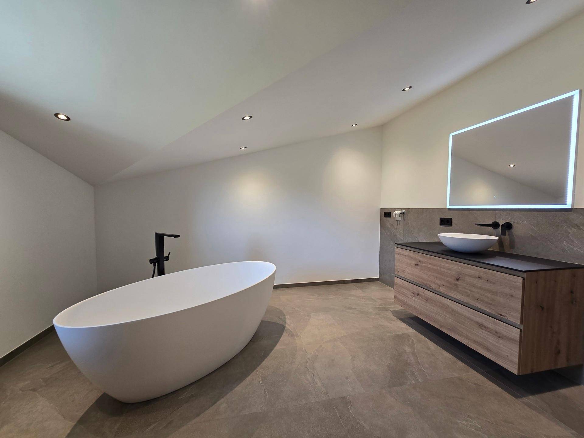Modernes Badezimmer mit freistehender Badewanne, schwebendem Waschtisch und beleuchtetem Spiegel.