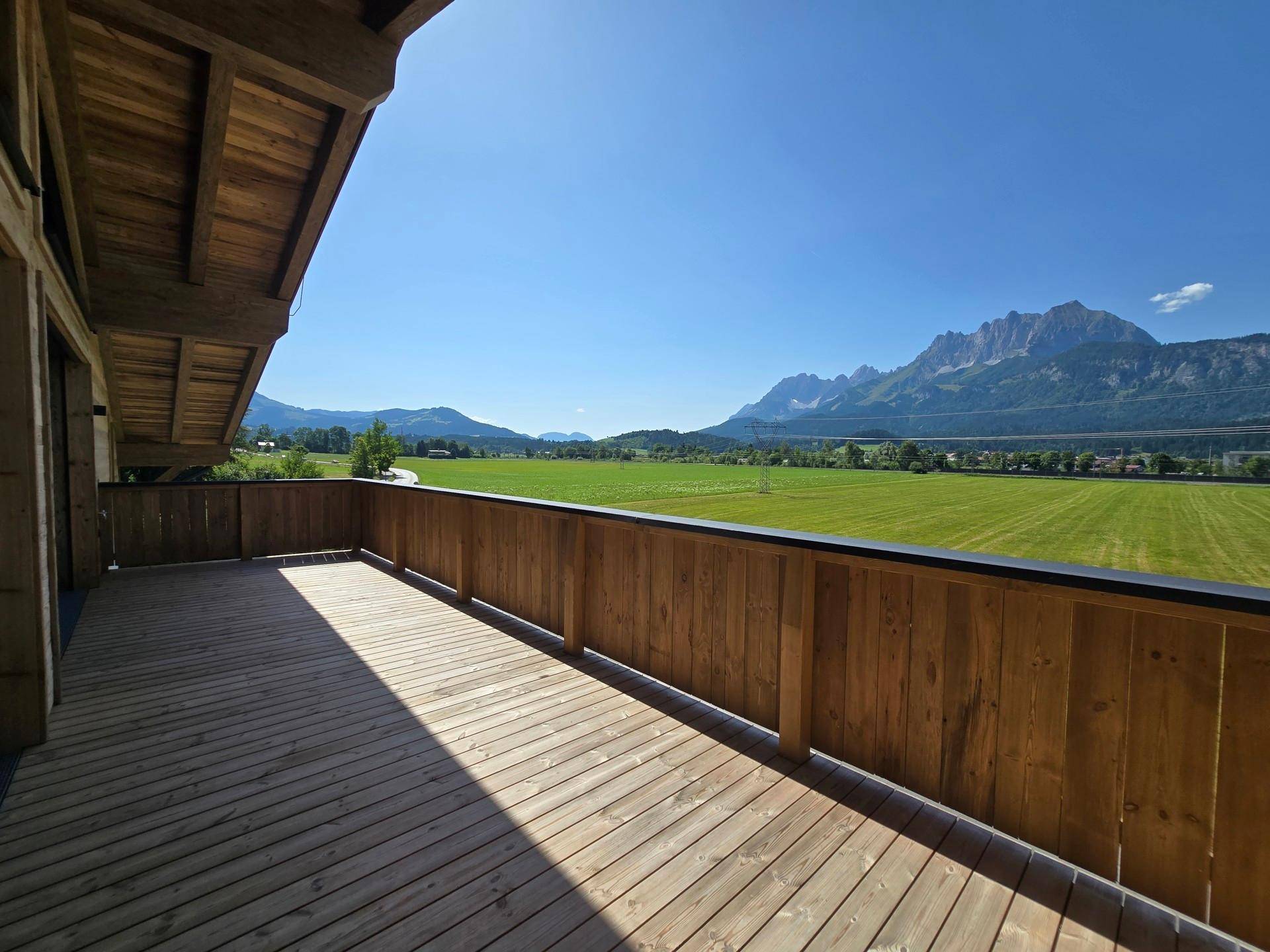 Großer Holzbalkon mit weitem Blick über grüne Felder und die umliegende Berglandschaft.