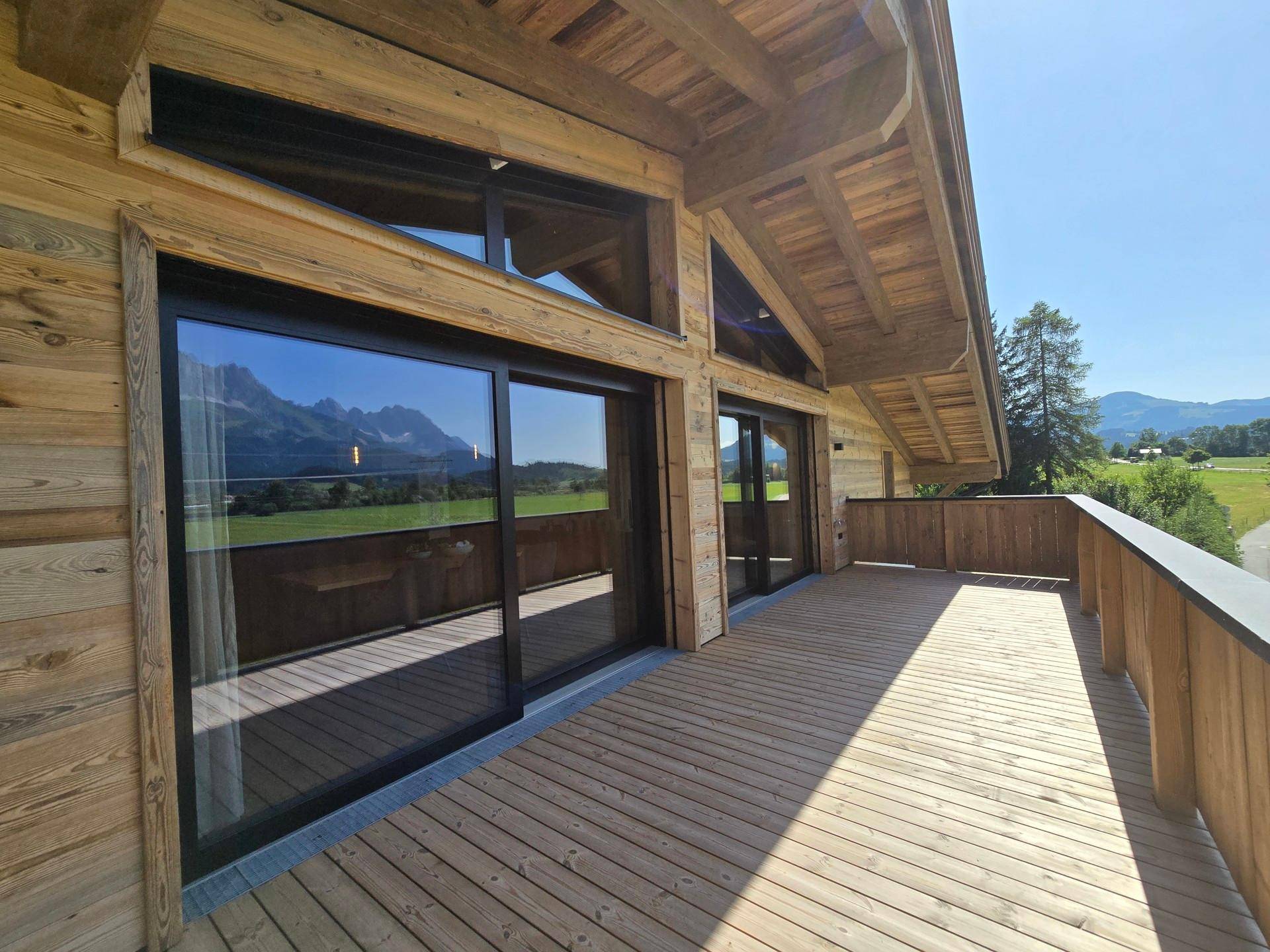 Holzfassade des Gebäudes mit großen Fenstern und einem weitläufigen Balkon mit Bergblick.