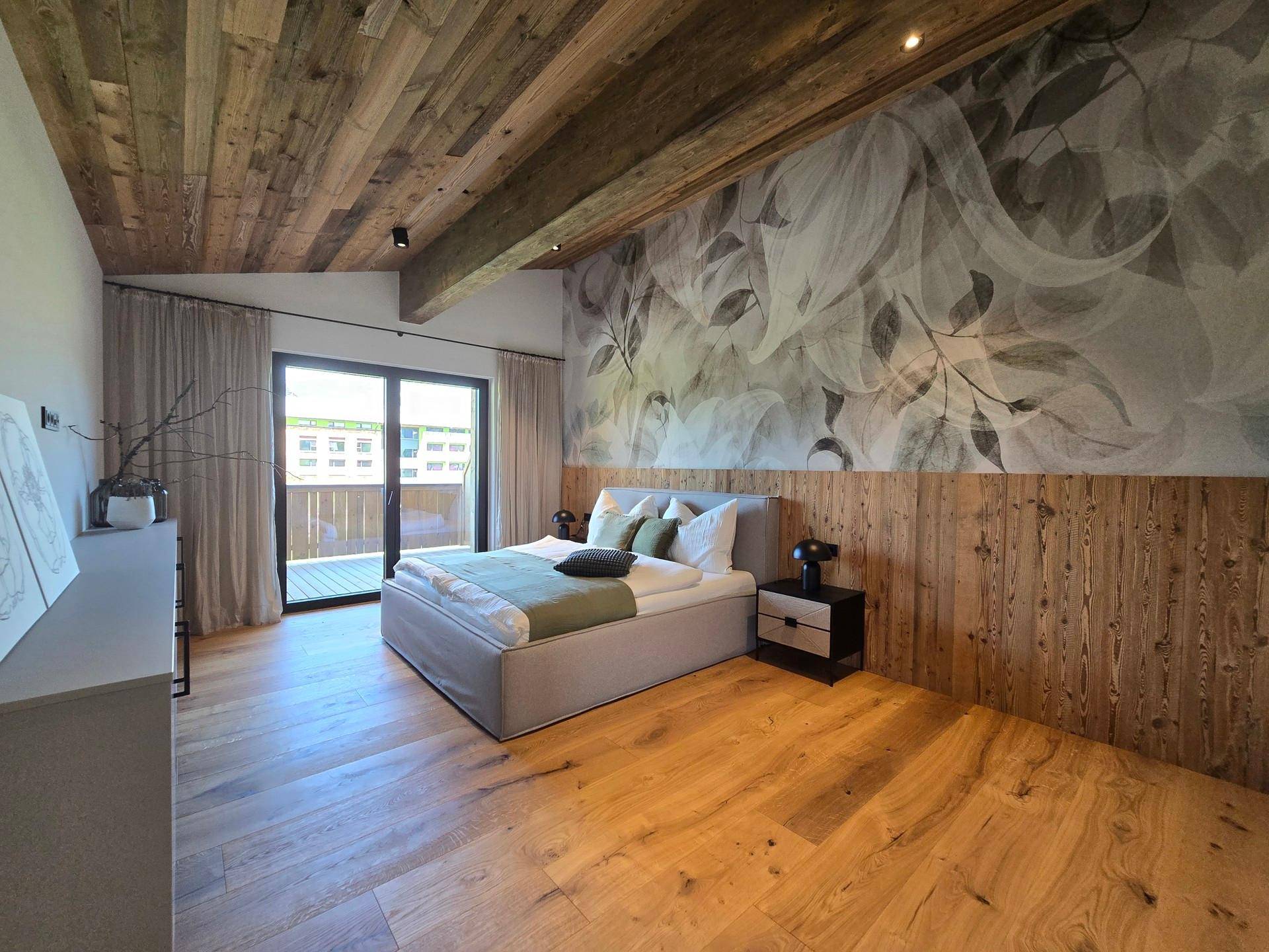 Gemütliches Schlafzimmer mit Holzboden, dekorativer Tapete und direktem Zugang zum Balkon.