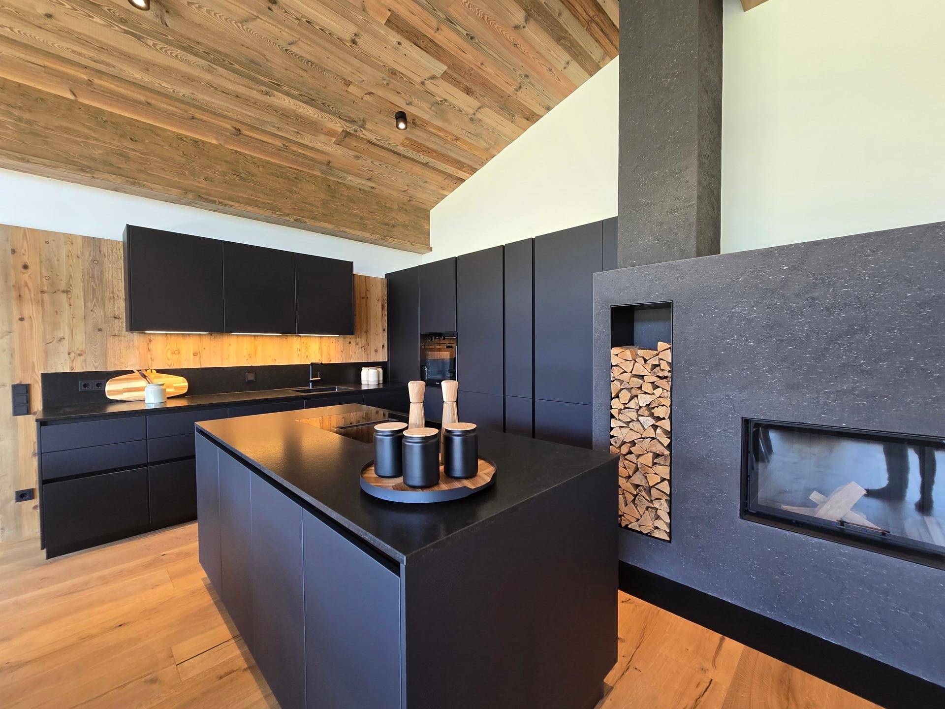 Moderne schwarze Küche mit Kochinsel, integrierten Geräten und einem stilvollen Kamin mit Holzfach.