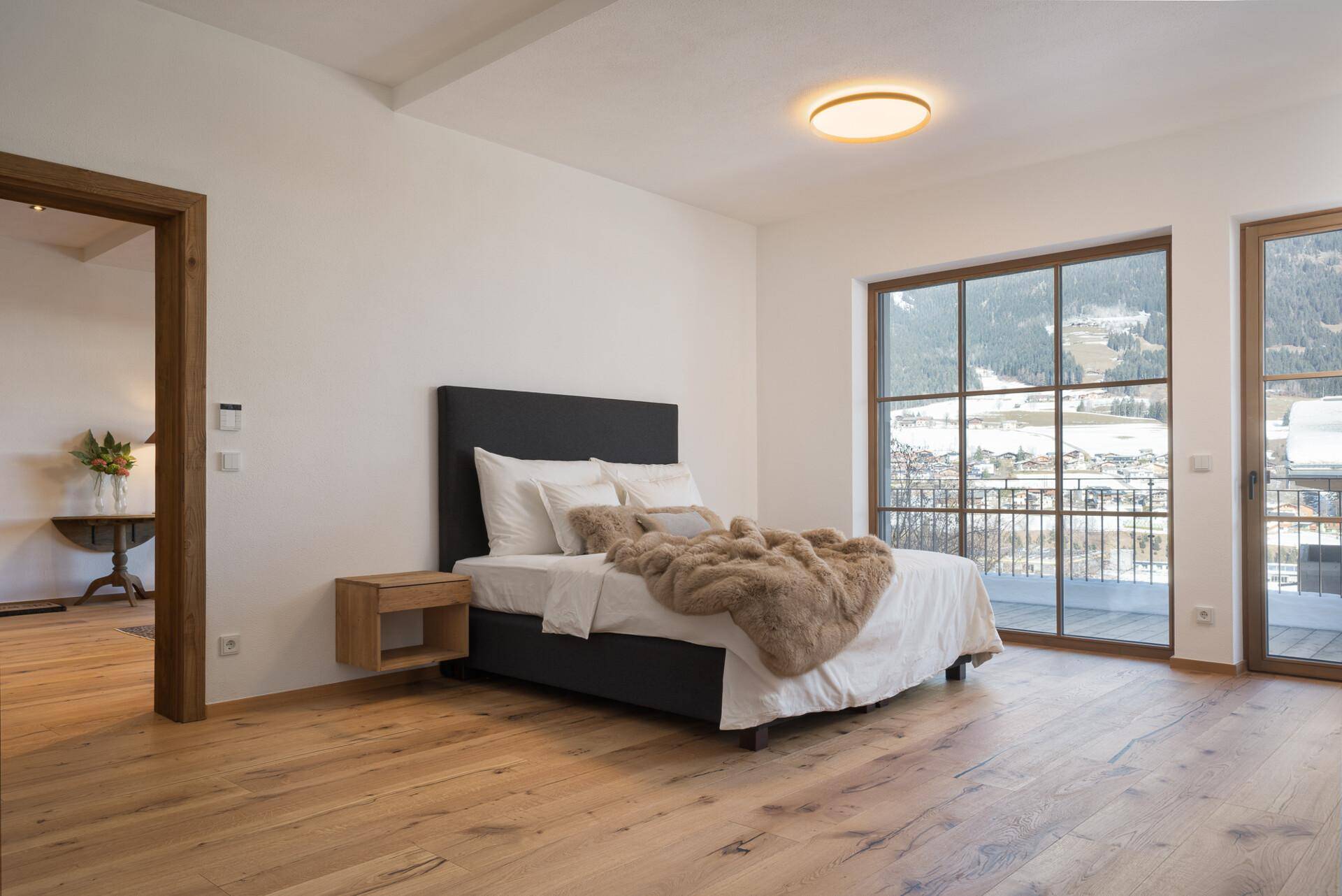 Helles Schlafzimmer mit Holzboden, großem Fenster und Zugang zu einem Balkon mit Bergblick.