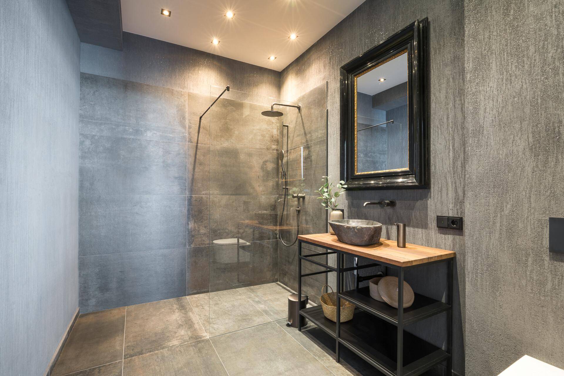 Modernes Badezimmer mit großer begehbarer Dusche, dunklen Fliesen und stilvollem Waschtisch.