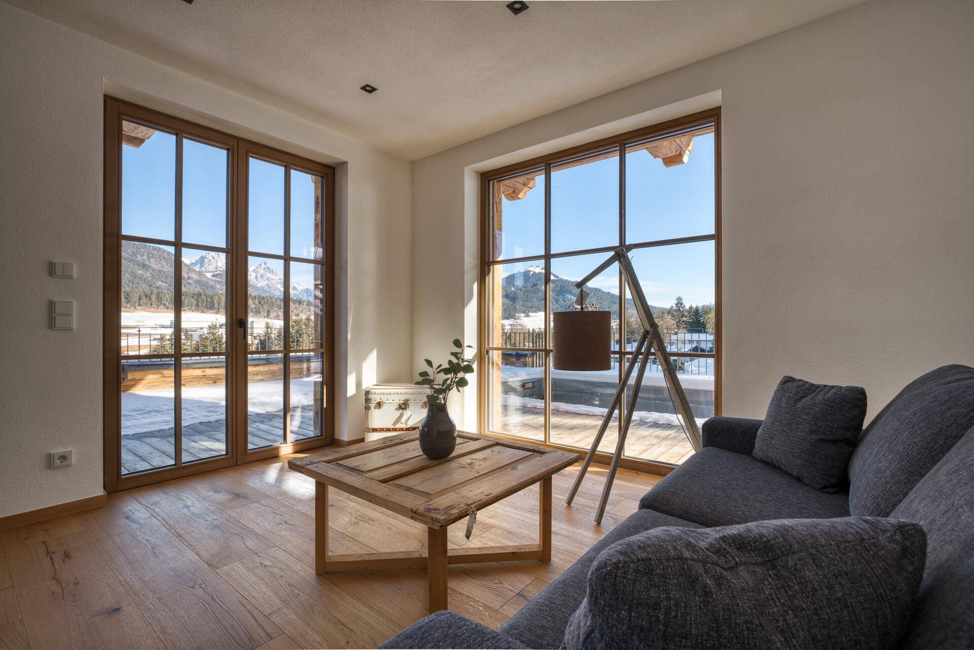 Gemütlicher Wohnbereich mit Sofa, Holzboden und großen Fenstern mit Bergblick.