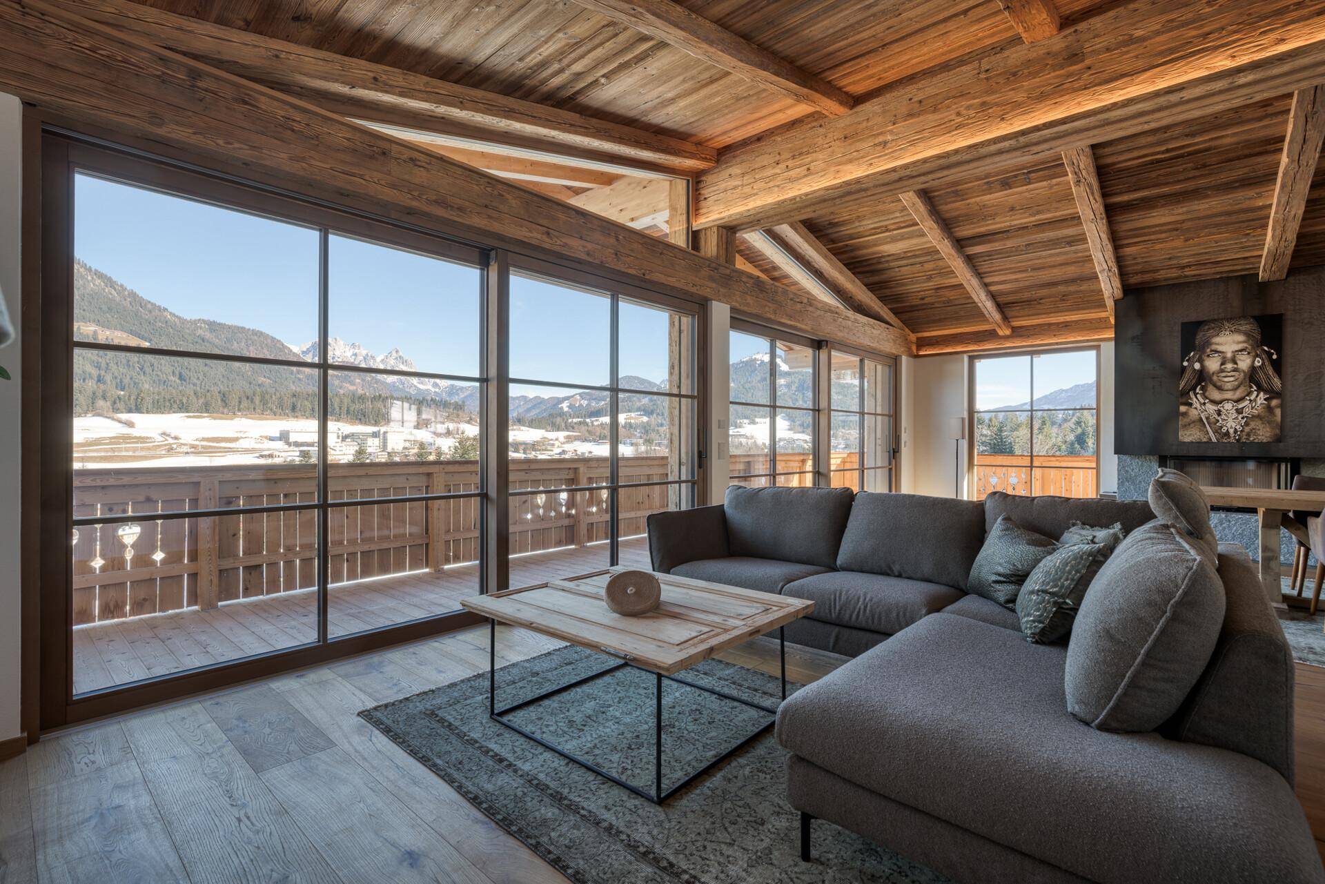 Gemütliches Wohnzimmer mit großem Sofa, Holzbalkendecke und weitem Blick auf die Berge.