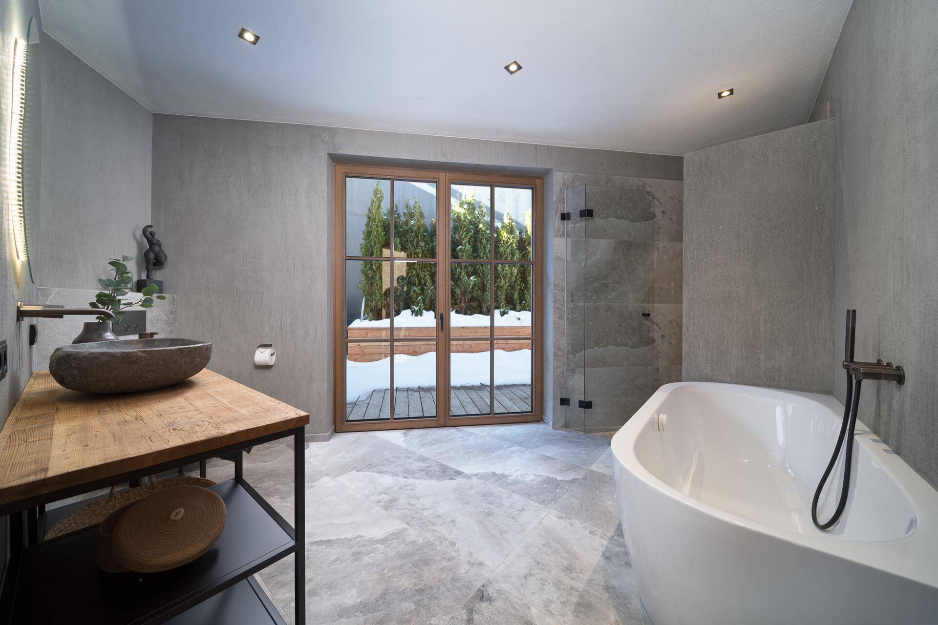 Modernes Badezimmer mit freistehender Badewanne, begehbarer Dusche und Zugang zu einem kleinen Außenbereich.