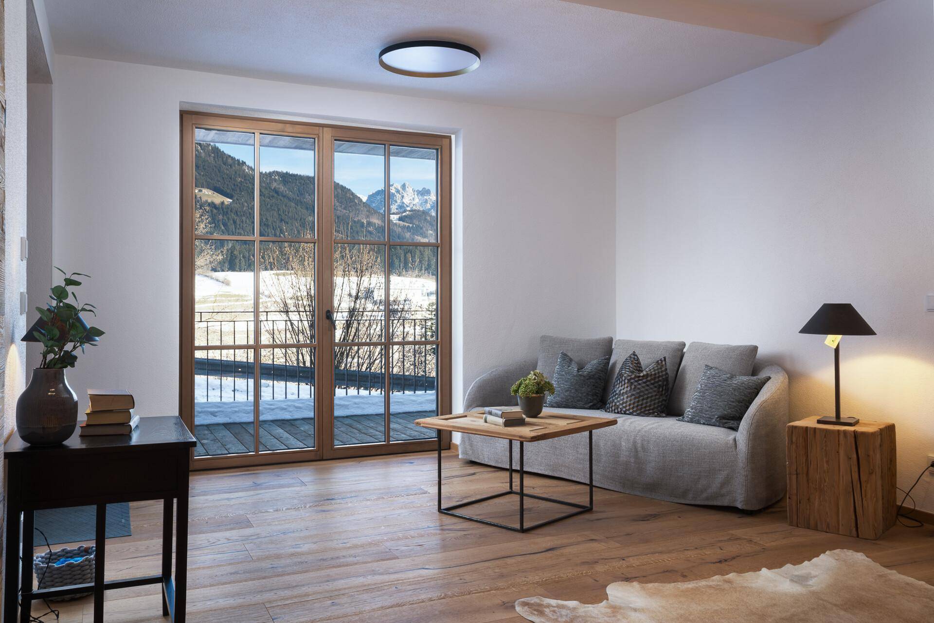 Helles Wohnzimmer mit bequemem Sofa, Holzboden und großen Fenstern, die einen weiten Bergblick bieten.