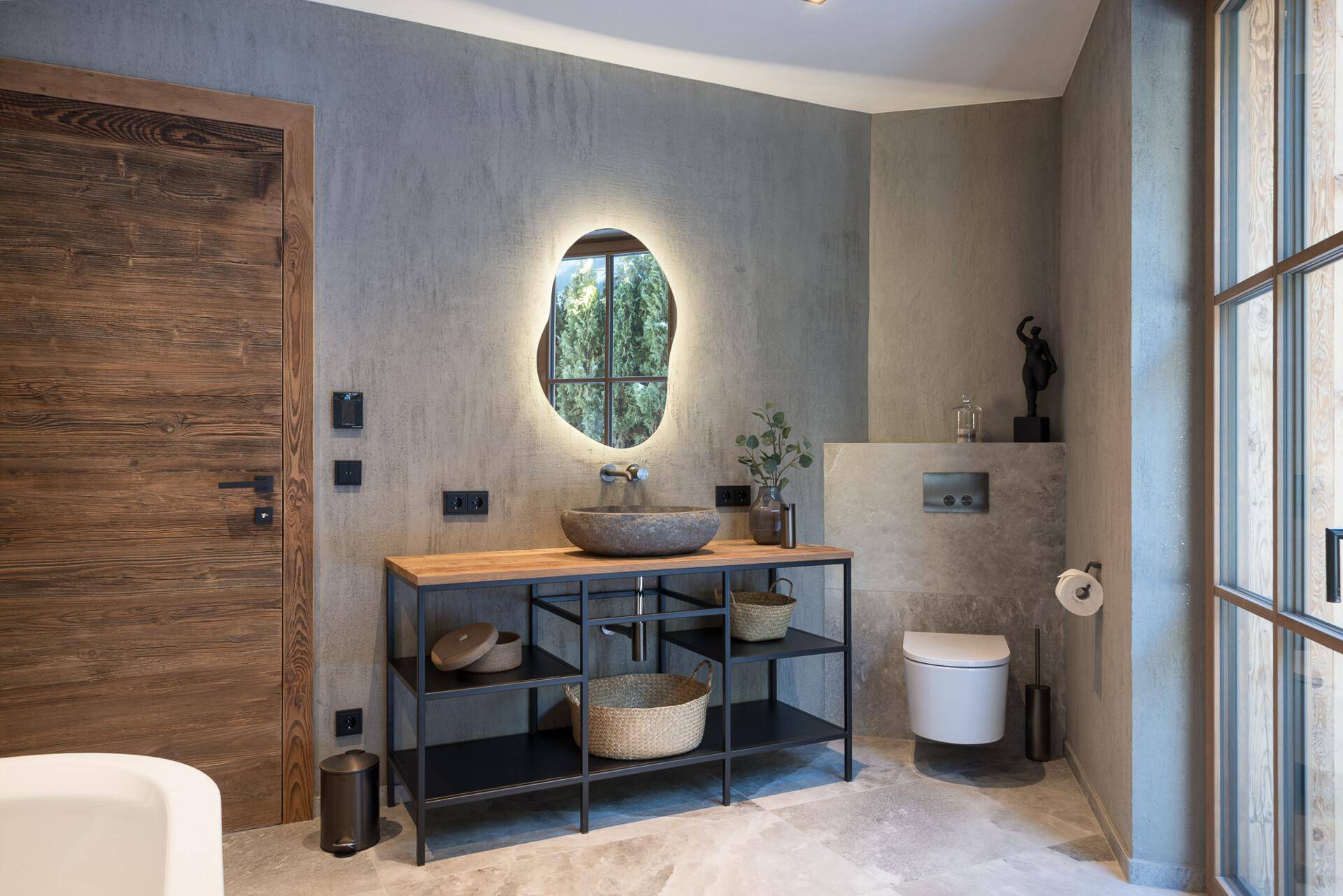 Stilvolles Badezimmer mit modernem Waschtisch, beleuchtetem Spiegel und wandhängendem WC in Grautönen.