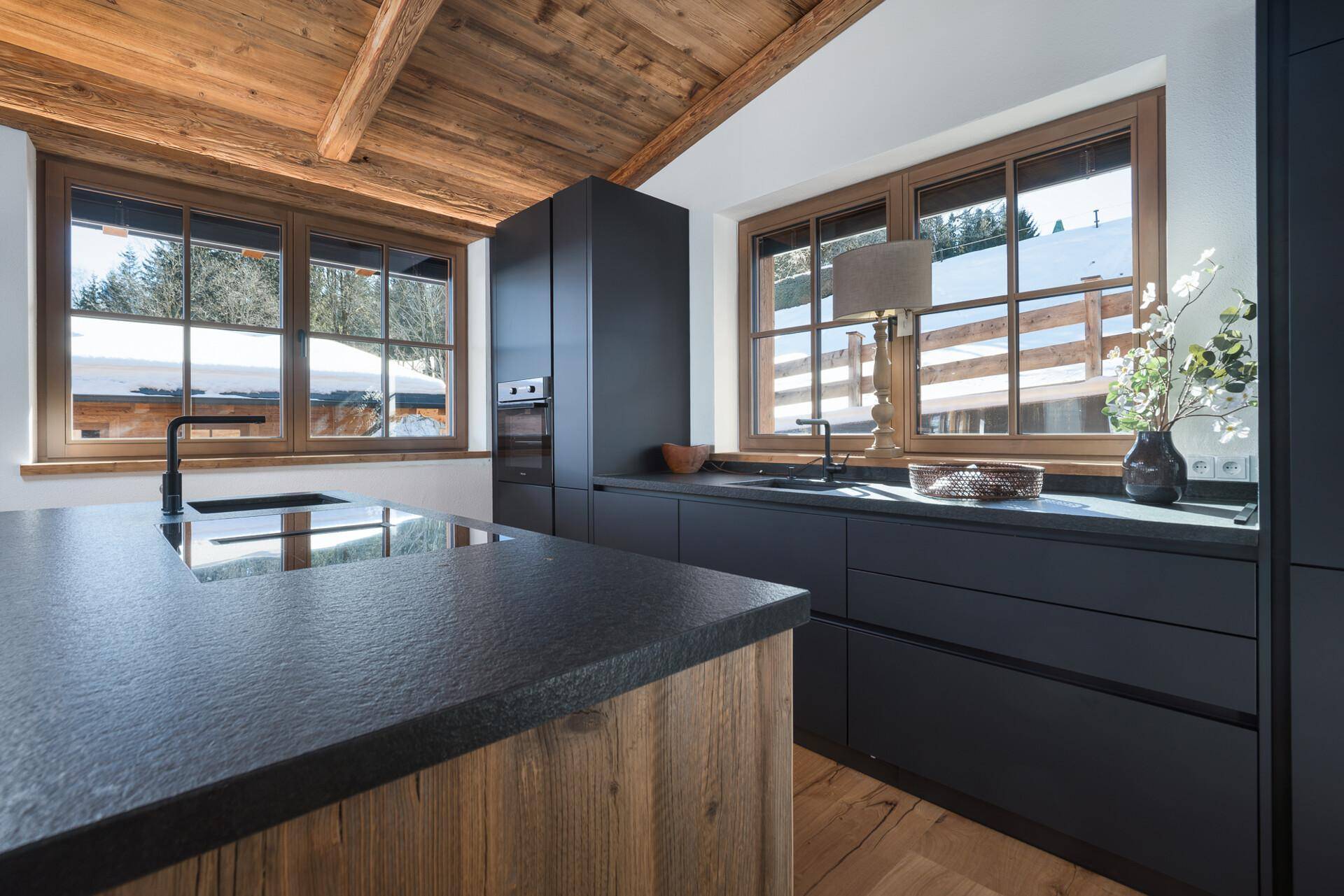 Moderne Küche mit schwarzen Schränken, Holzdetails und einer Kücheninsel, die zum Kochen und Verweilen einlädt.