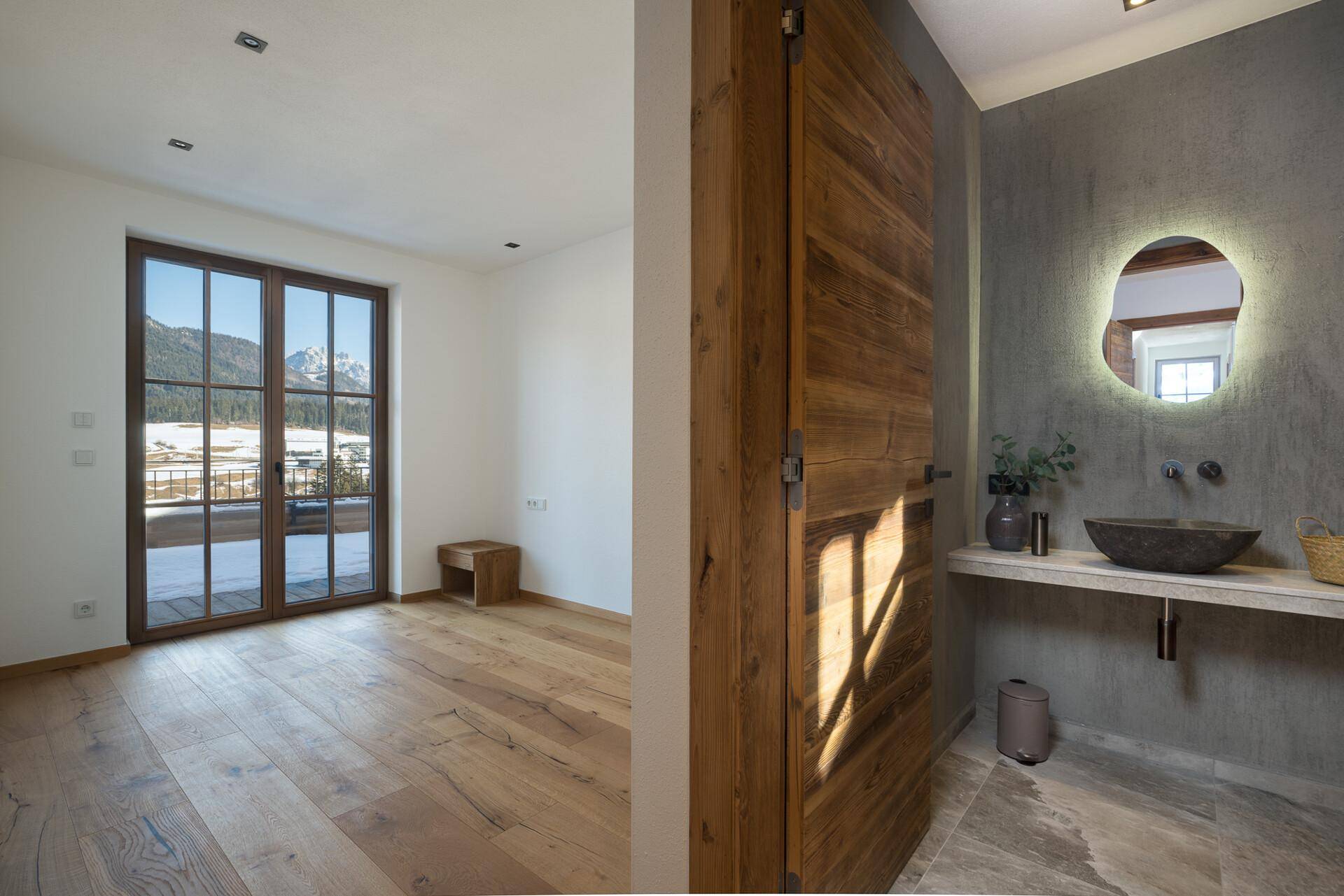 Helles Schlafzimmer mit Holzboden, großen Fenstern und einem atemberaubenden Bergblick, mit Badzugang.