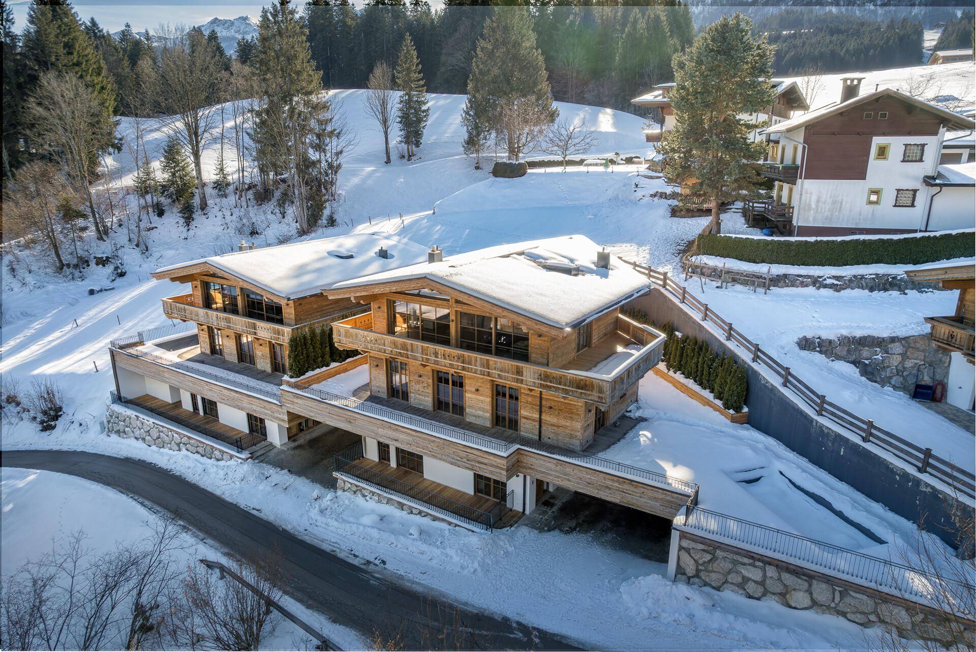 Moderne Chalet-Anlage in einer verschneiten Berglandschaft, mit Holzfassaden und großzügigen Balkonen.
