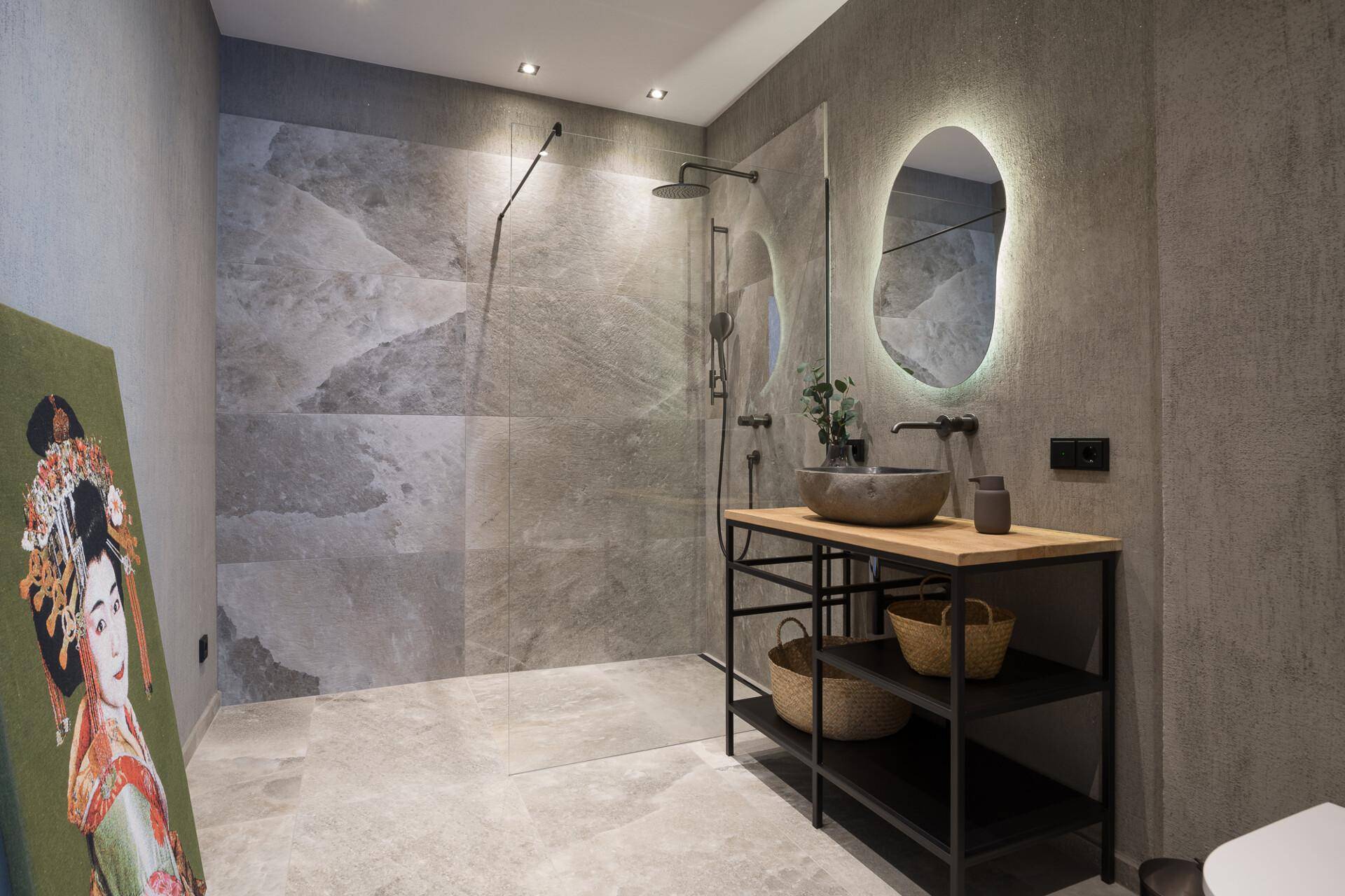 Modernes Badezimmer mit begehbarer Dusche, stilvollem Waschtisch und beleuchtetem Spiegel, in eleganten Grautönen gehalten.