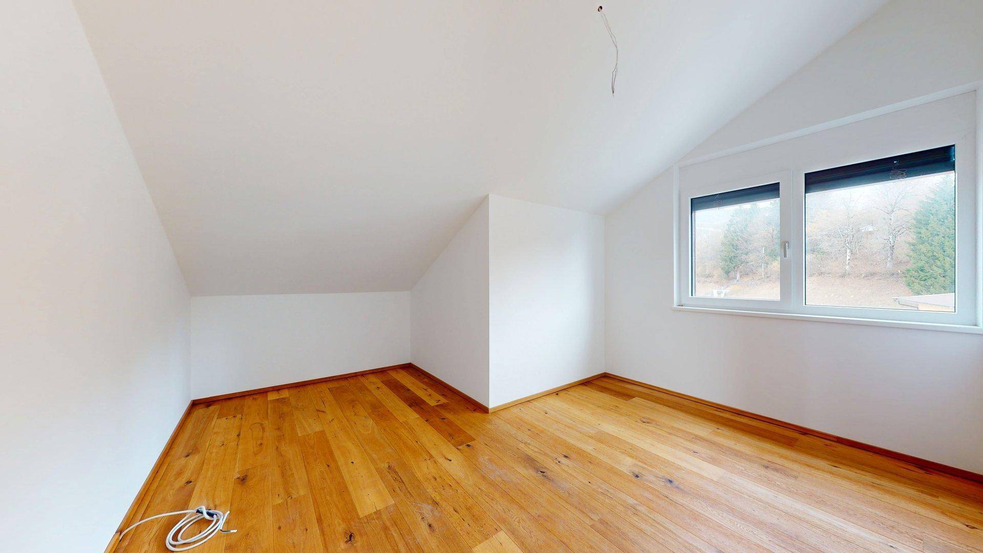 Gemütliches Zimmer mit Holzboden, Dachschräge und Fenster mit Blick auf die Natur.
