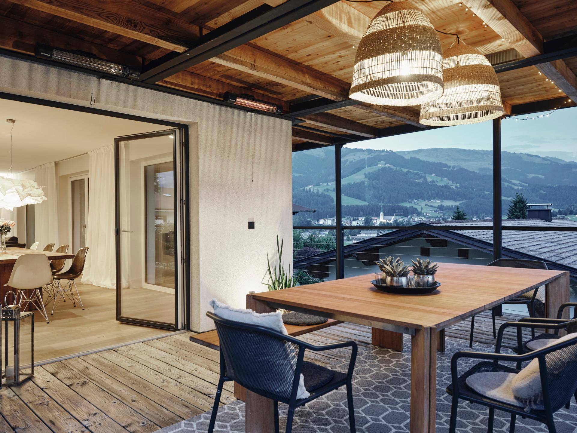 Stilvolle überdachte Terrasse mit Holzboden und Blick auf die beleuchtete Berglandschaft am Abend.