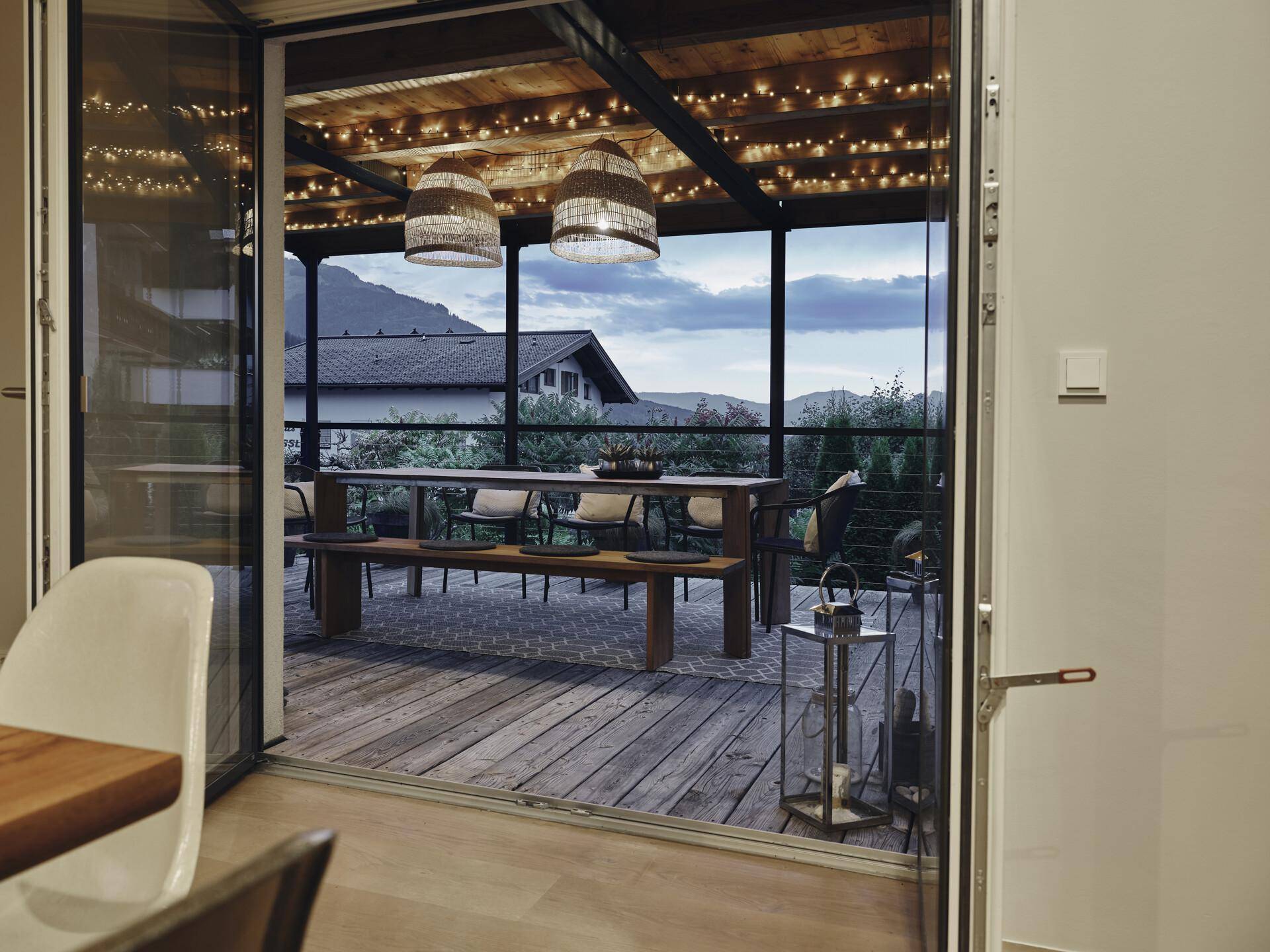 Heller Innenraum mit Zugang zur Terrasse und weitem Blick auf die abendliche Berglandschaft.