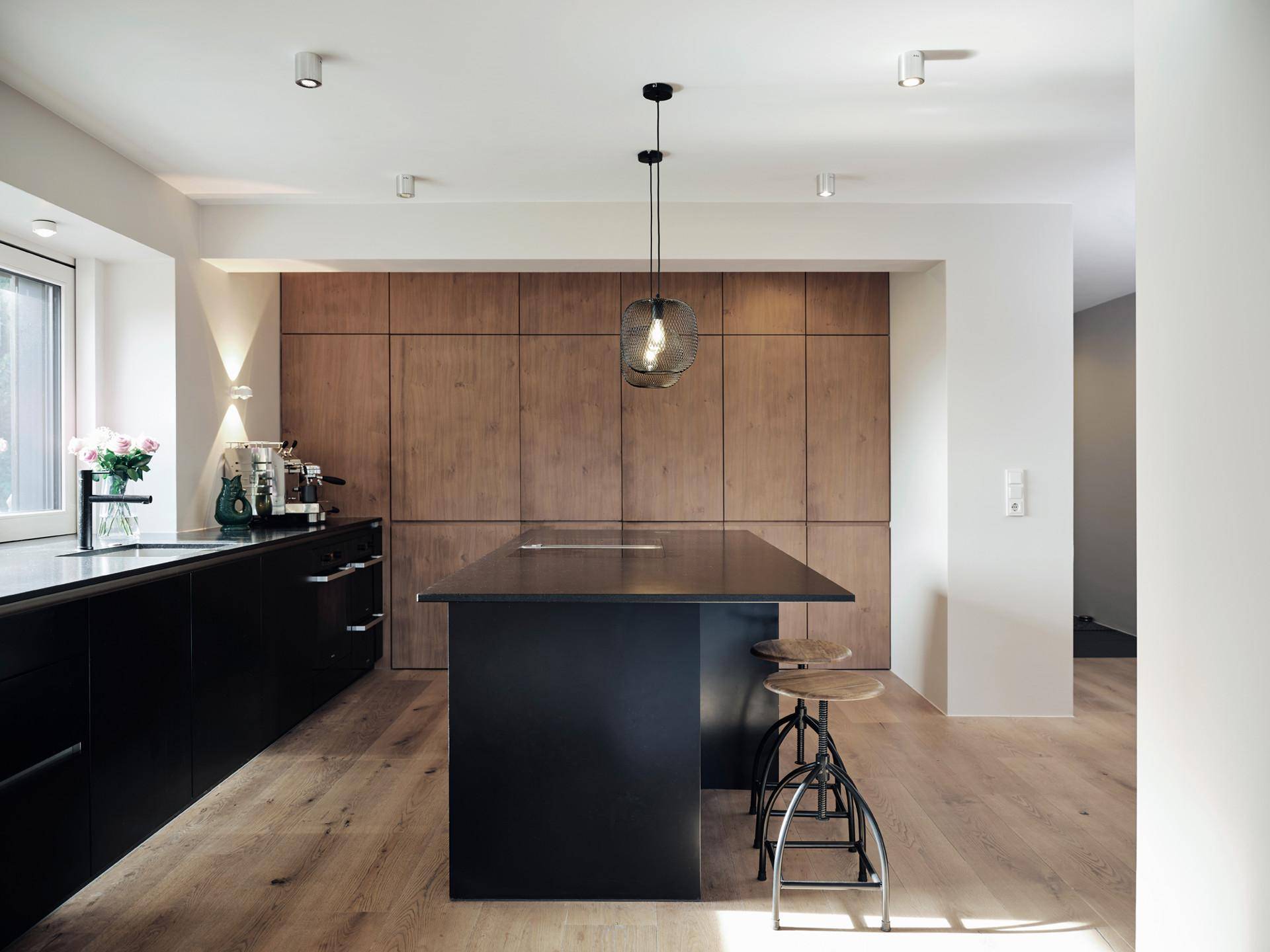 Moderne Küche mit schwarzer Kücheninsel, Holzwand und integrierten Geräten, hell beleuchtet.