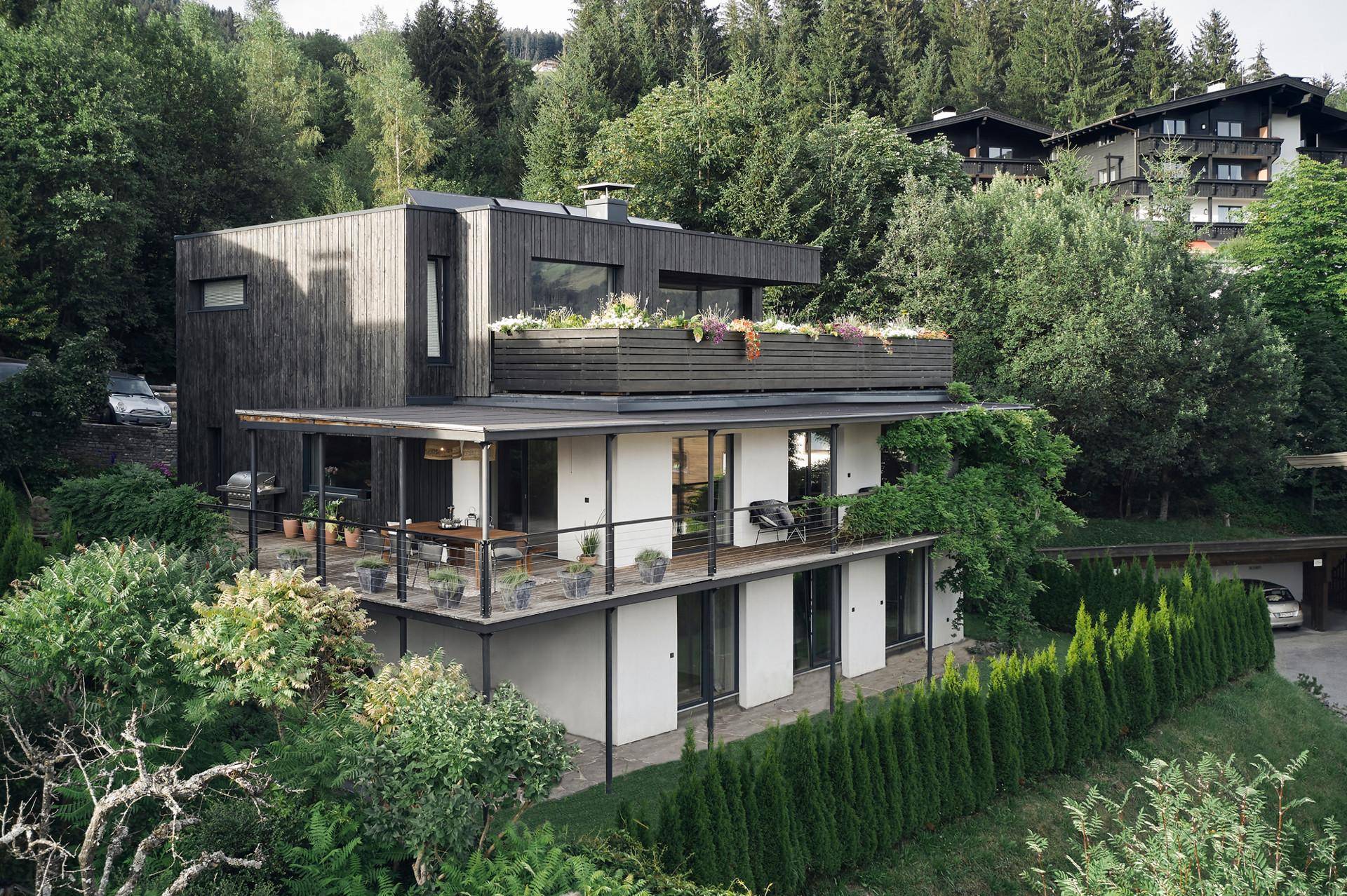 Modernes Wohnhaus mit mehreren Terrassen und Balkonen, eingebettet in eine grüne, bewaldete Umgebung.