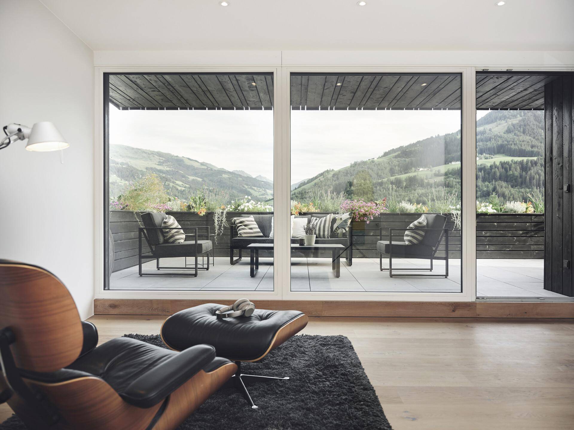 Gemütlicher Wohnbereich mit Design-Sessel und großen Fenstern mit Bergblick und Terrassenzugang.