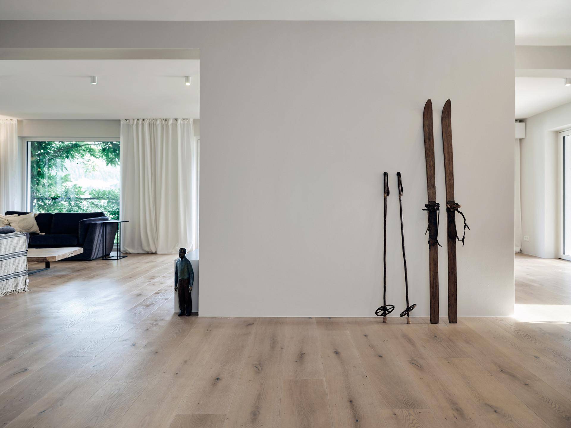 Heller Flurbereich mit Holzboden und dekorativen Holzskiern, der zu einem Wohnbereich führt.