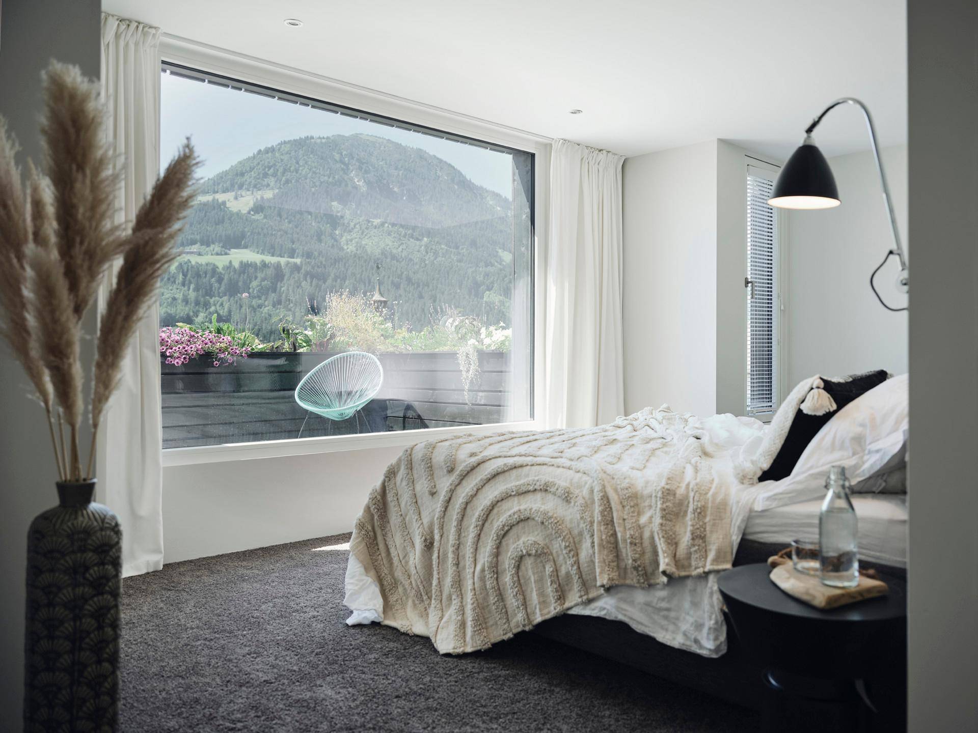 Helles Schlafzimmer mit großem Fenster, Teppichboden und weitem Blick auf die Berge.