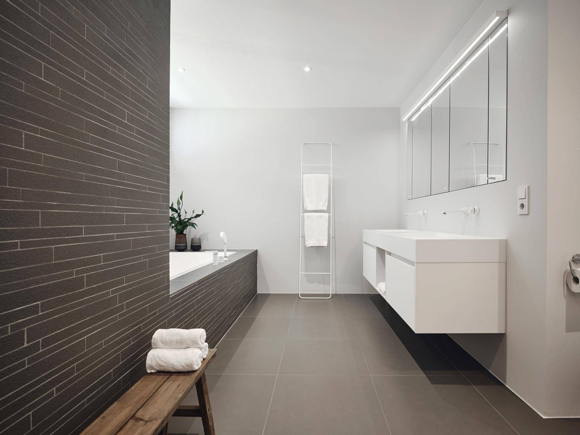 Modernes Badezimmer mit Doppelwaschbecken, Badewanne und eleganten dunklen Fliesen.