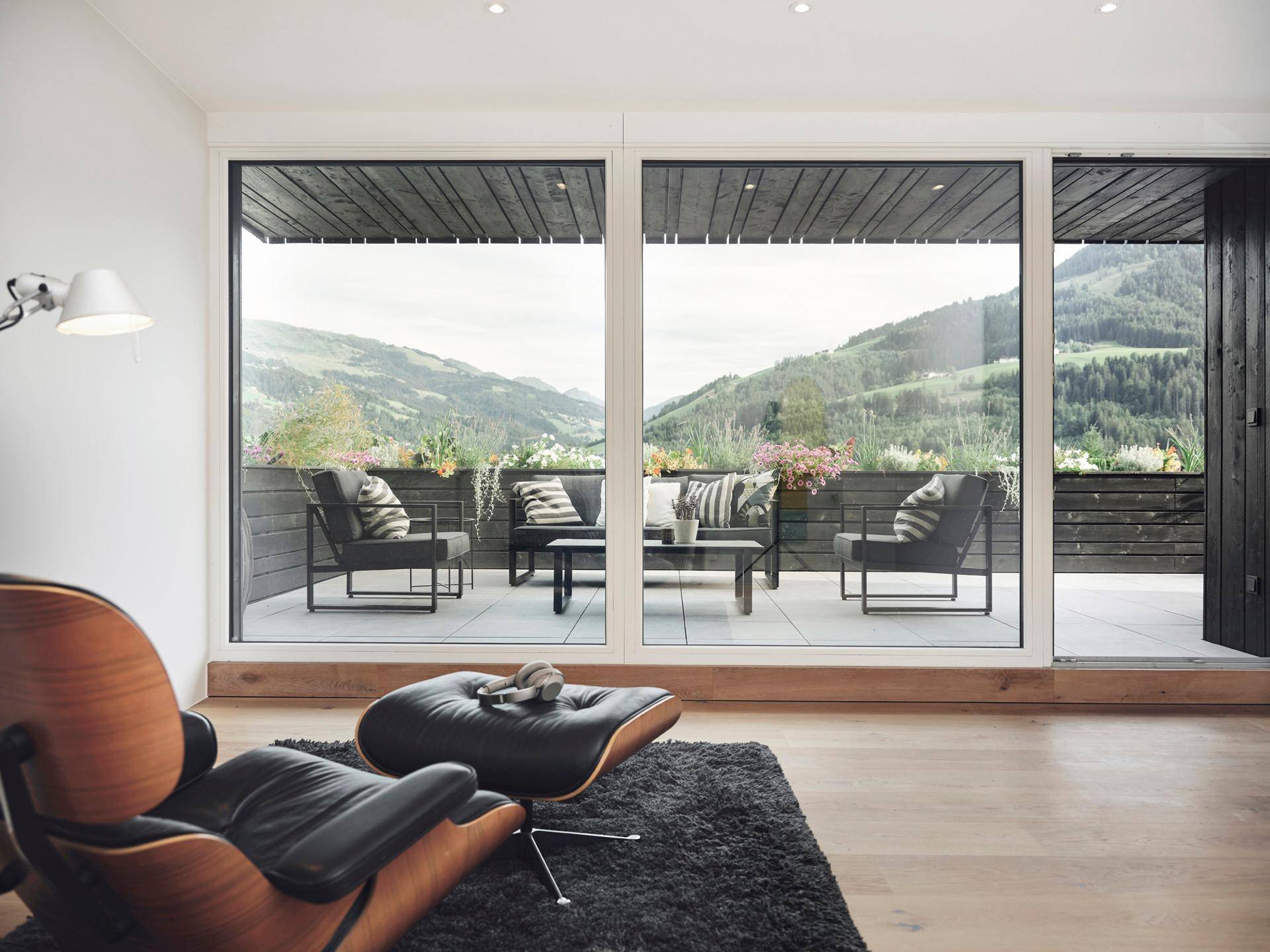 Gemütlicher Wohnbereich mit Design-Sessel und großen Fenstern mit Bergblick und Terrassenzugang.