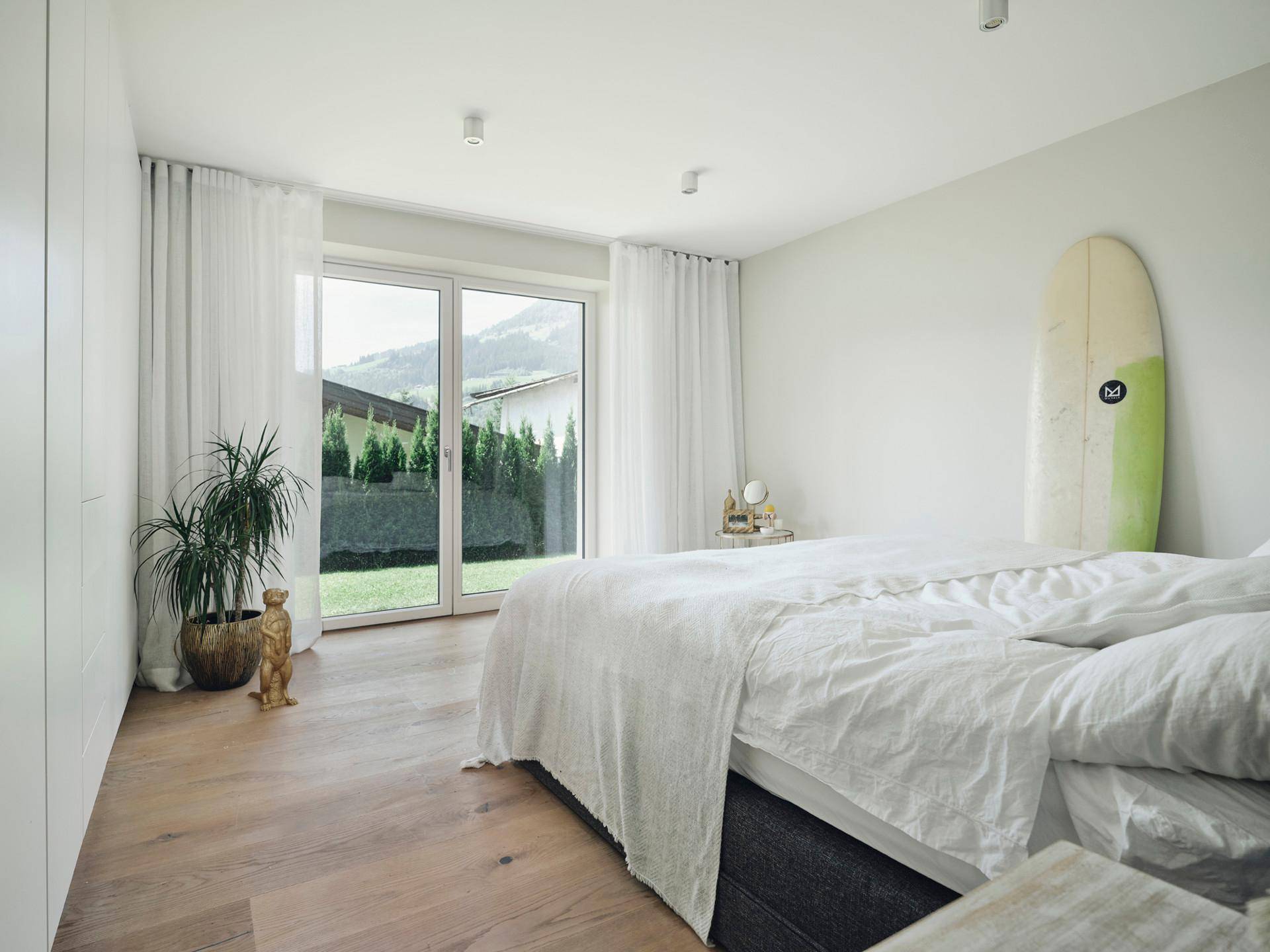 Helles Schlafzimmer mit Holzboden und großen Fenstern mit Zugang zum Garten und Blick ins Grüne.