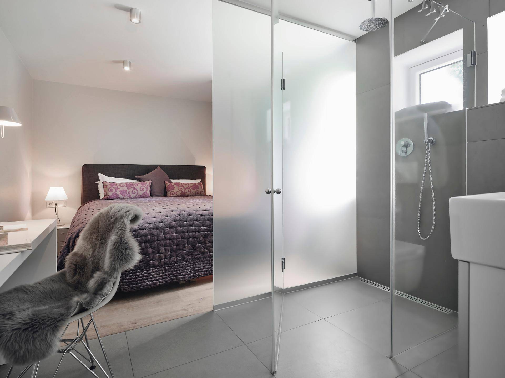 Modernes Badezimmer mit begehbarer Dusche und direktem Zugang zu einem Schlafzimmer.