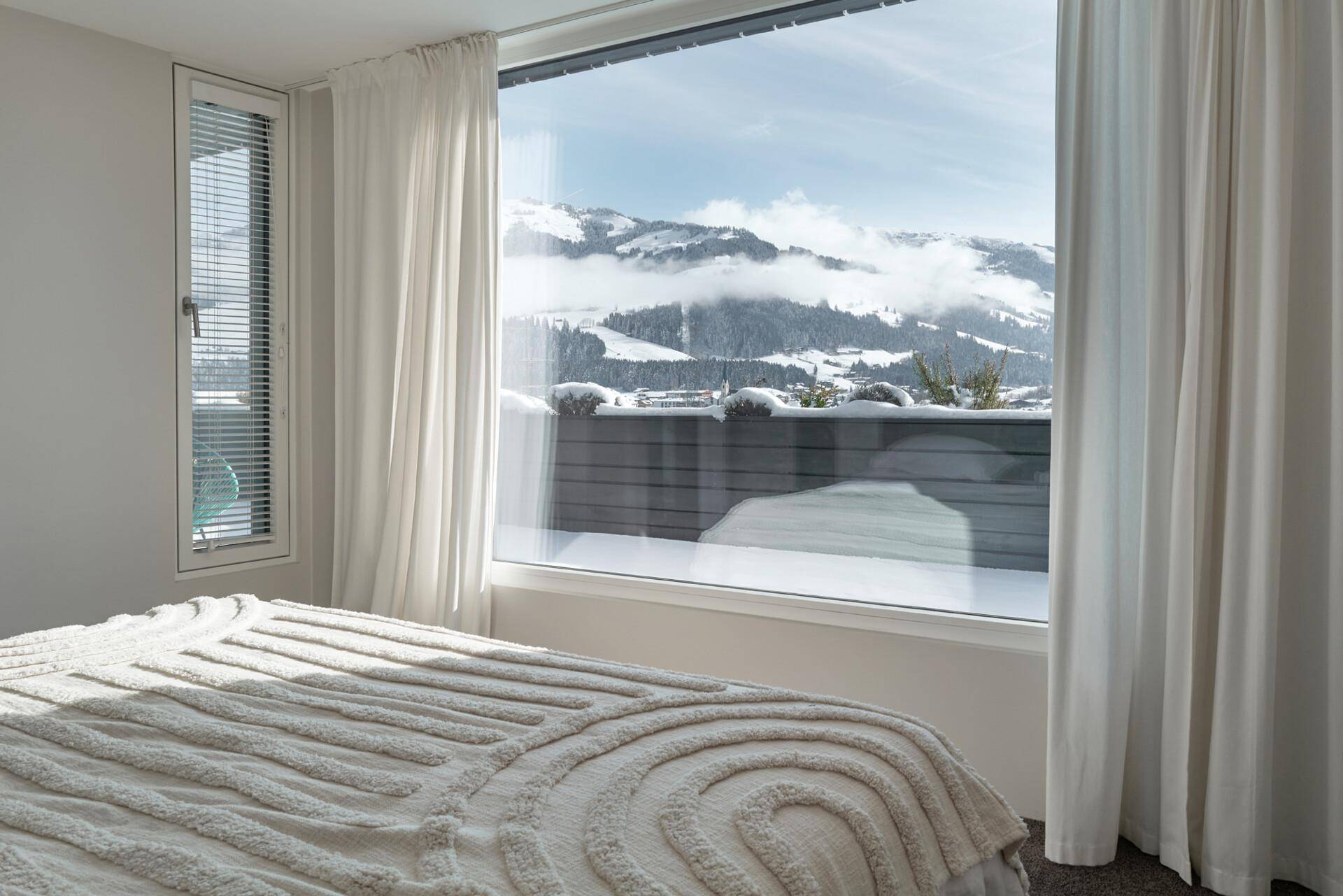 Gemütliches Schlafzimmer mit großem Fenster und atemberaubendem Blick auf die verschneite Berglandschaft.