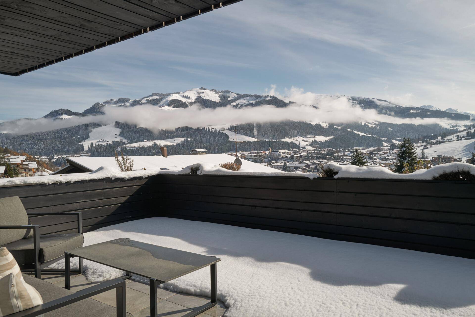 Verschneite Terrasse mit Loungemöbeln und weitem Blick auf die winterliche Berglandschaft.