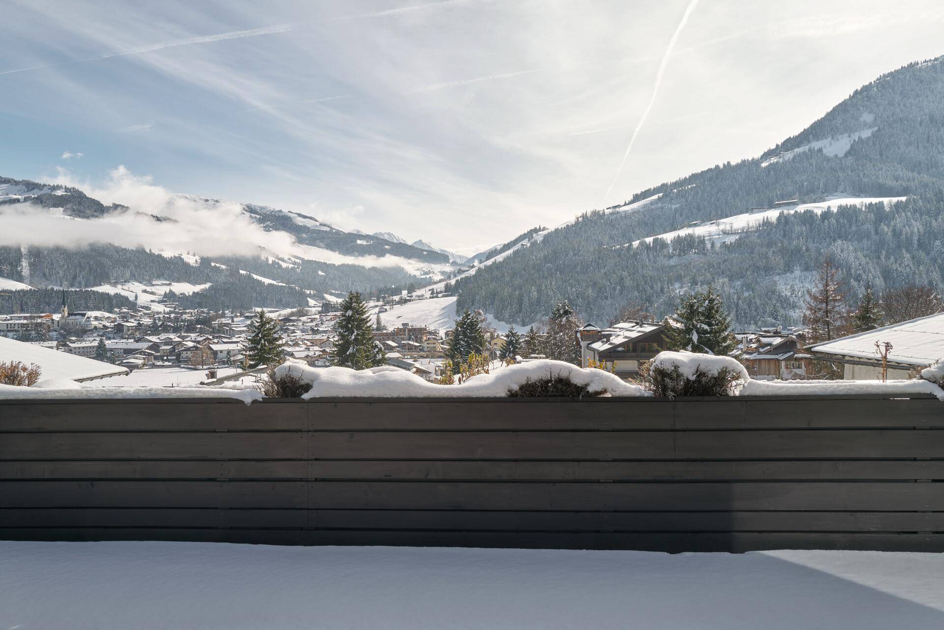 Panoramablick auf ein verschneites Dorf und die umliegenden Berge an einem klaren Wintertag.