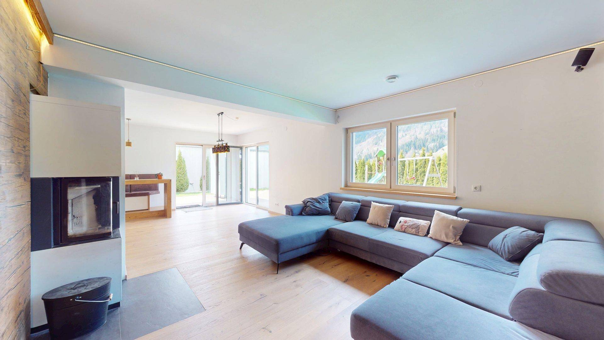 Gemütliches Wohnzimmer mit großem Ecksofa, Kamin und Blick auf die umliegende Berglandschaft.