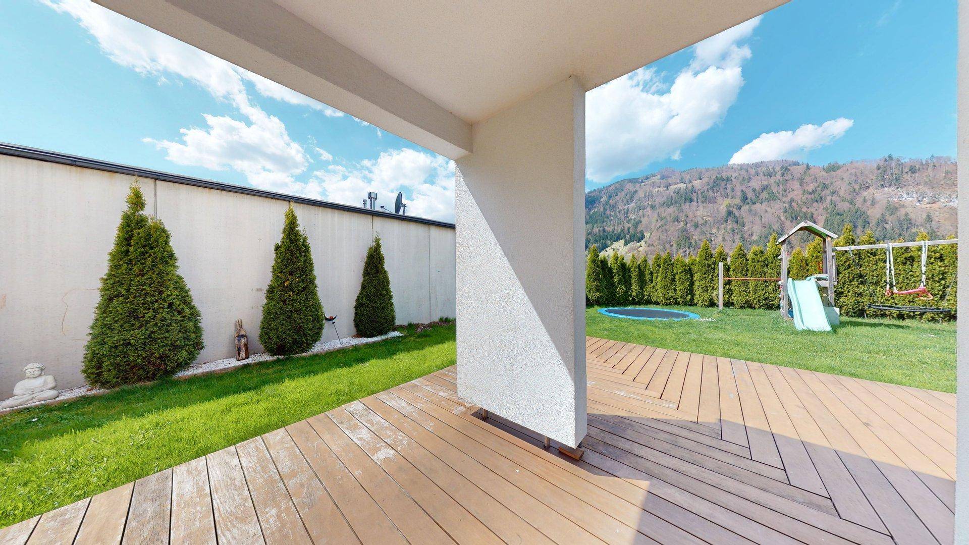 Geräumige überdachte Terrasse mit Holzboden und Blick auf den Garten und die Berge.