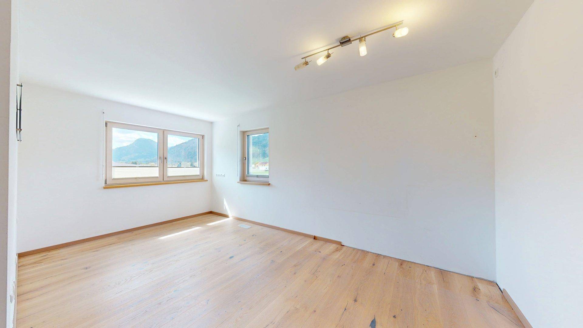 Helles Schlafzimmer mit Holzboden und großen Fenstern, die viel Tageslicht hereinlassen.