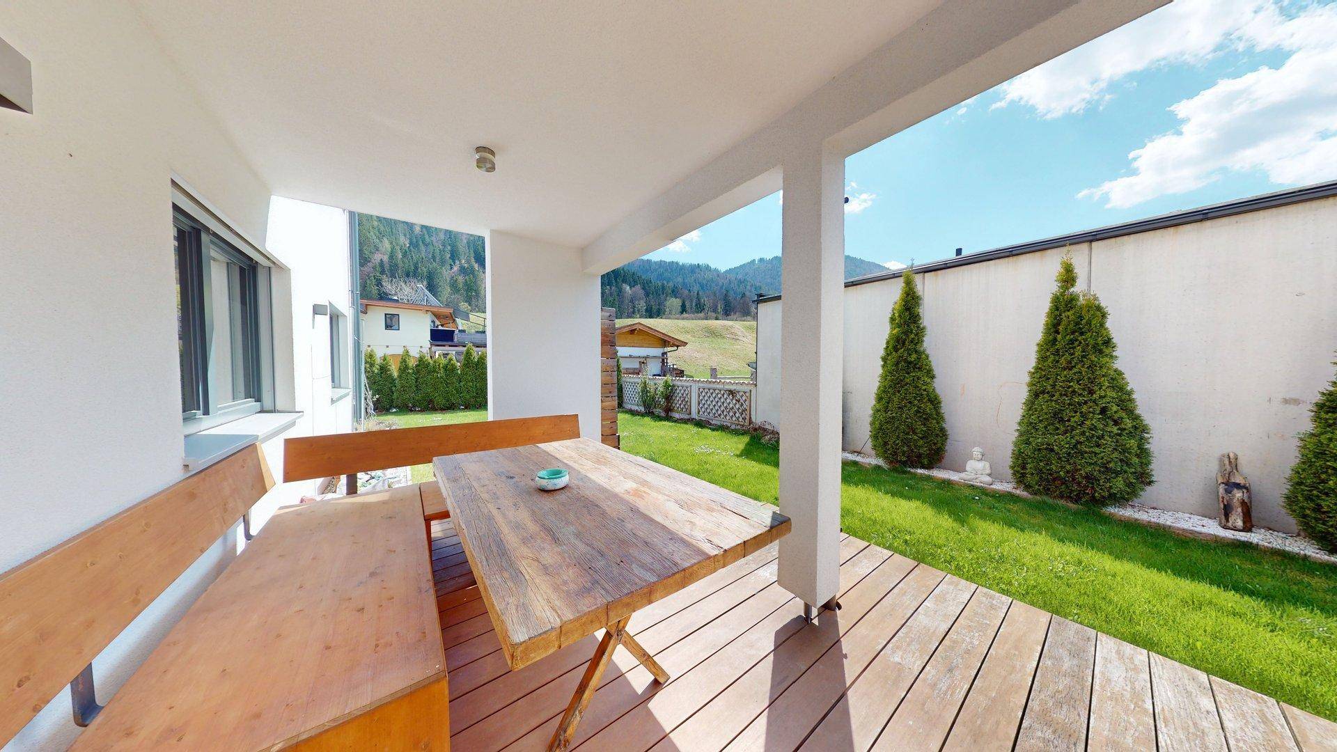 Überdachte Terrasse mit Holztisch und Bänken, ideal für Mahlzeiten im Freien mit Gartenblick.
