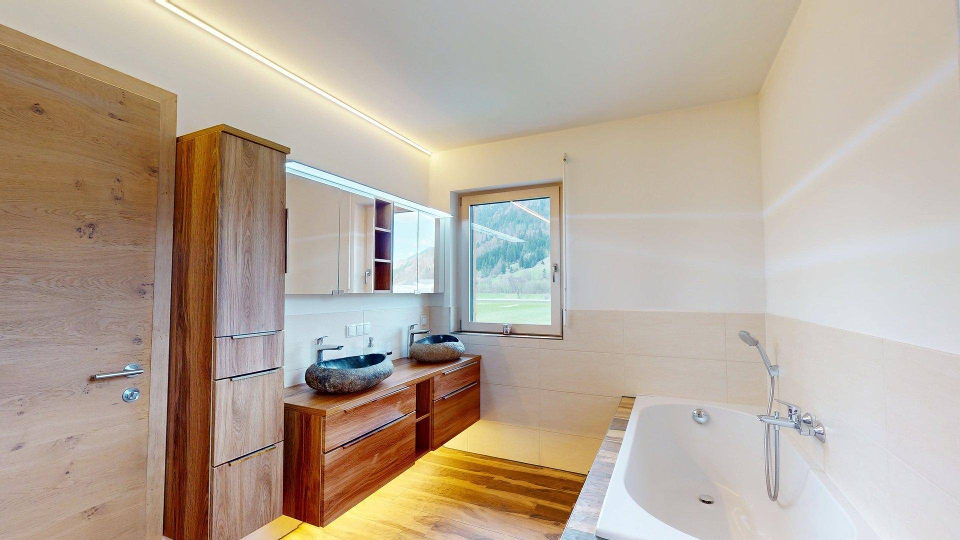 Geräumiges Badezimmer mit zwei Steinwaschbecken, Badewanne und Fenster mit Bergblick.