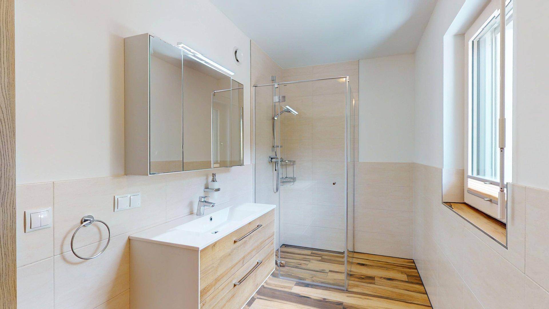 Funktionales Badezimmer mit Dusche, Waschtisch und Fenster, das viel Tageslicht spendet.