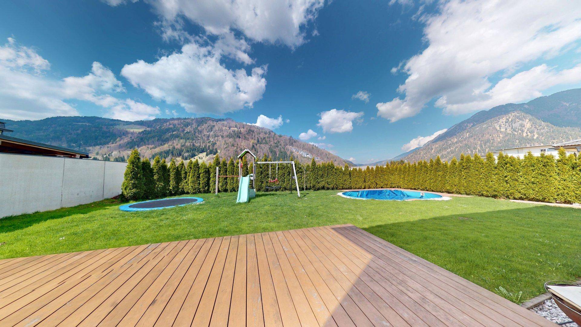 Weitläufiger Garten mit Spielgeräten, Pool und herrlichem Bergblick unter blauem Himmel.