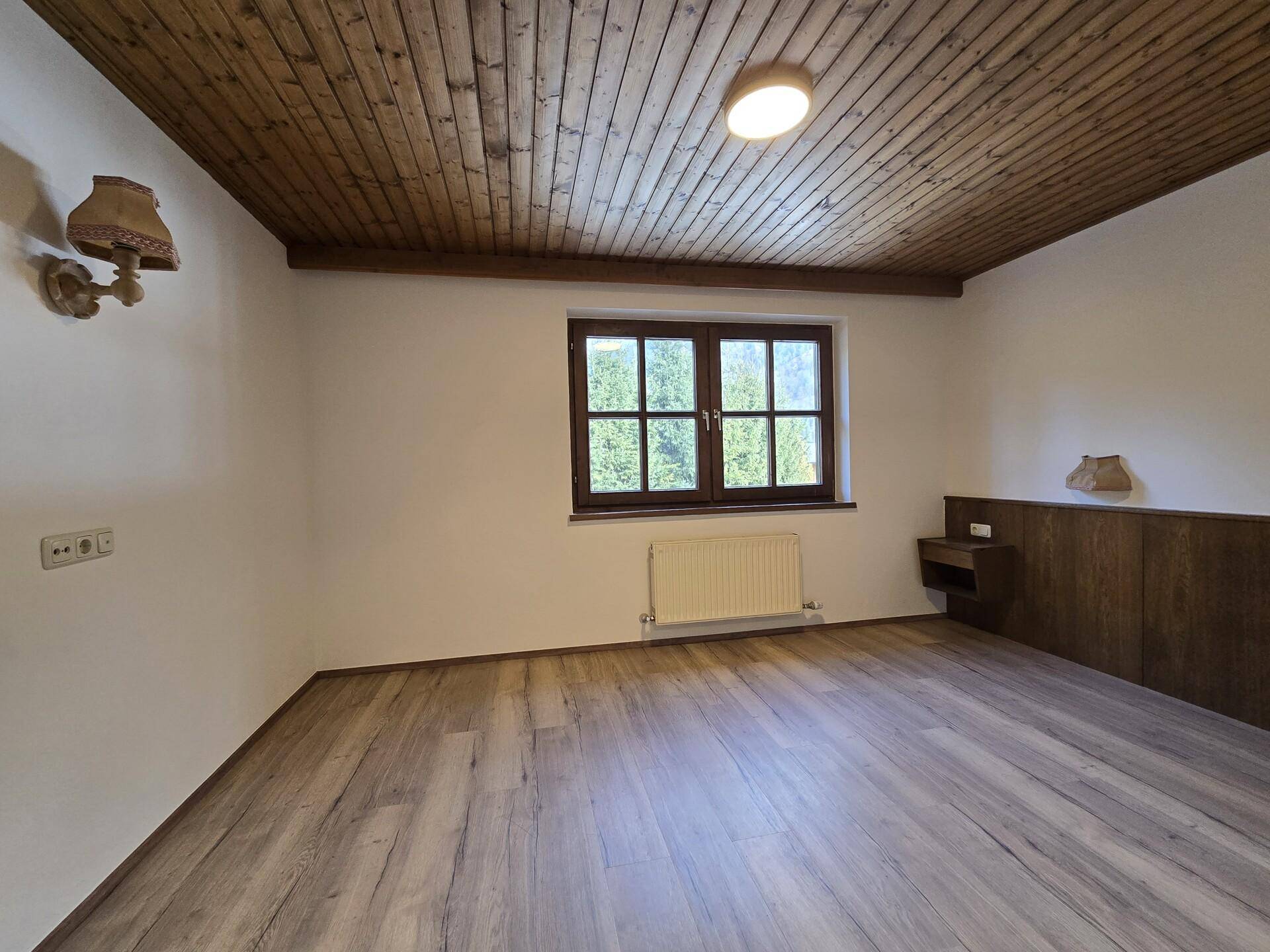 Schlafzimmer mit Holzbalkendecke, Laminatboden und Fenster mit Bergblick.