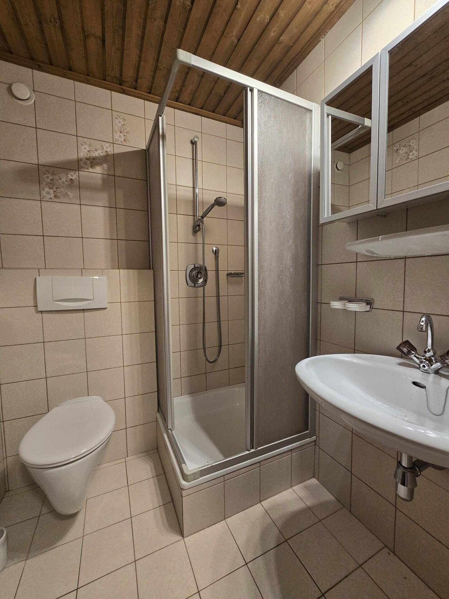 Badezimmer mit Duschkabine, WC, Waschbecken und hellen Fliesen.