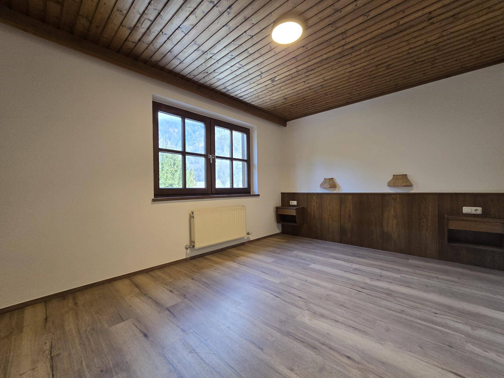 Geräumiges Schlafzimmer mit Holzbalkendecke, Laminatboden und Fenster.