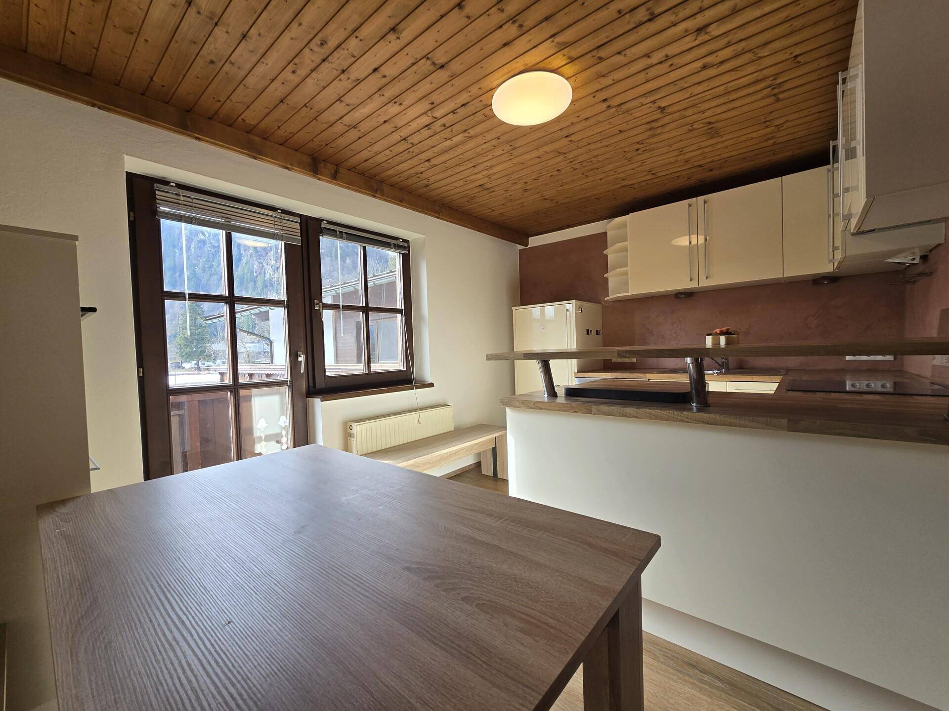 Kleine Küche mit Holztisch, Einbauschränken und Zugang zum Balkon.