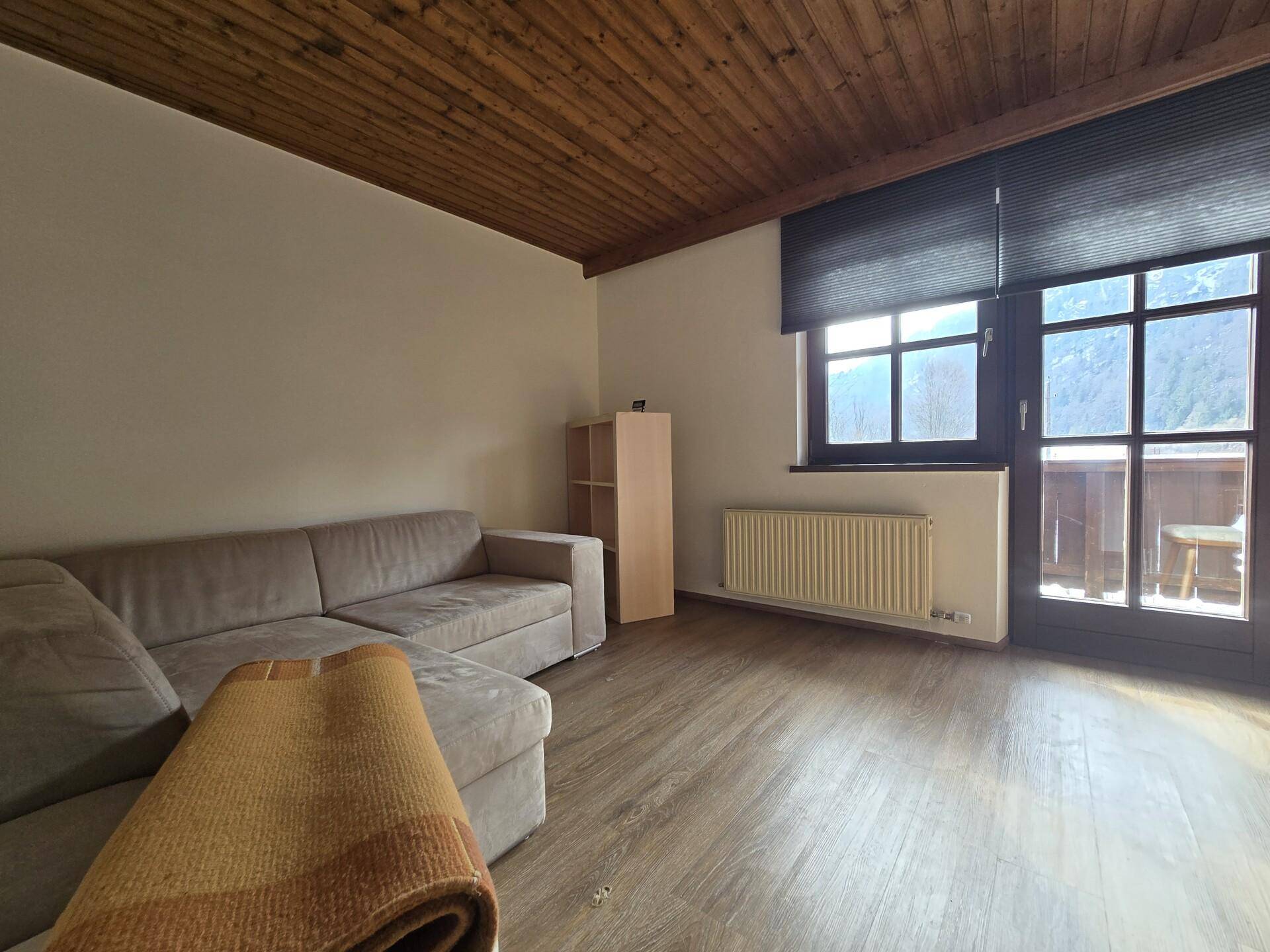 Wohnzimmer mit Sofa, Laminatboden und Zugang zu einem kleinen Balkon.