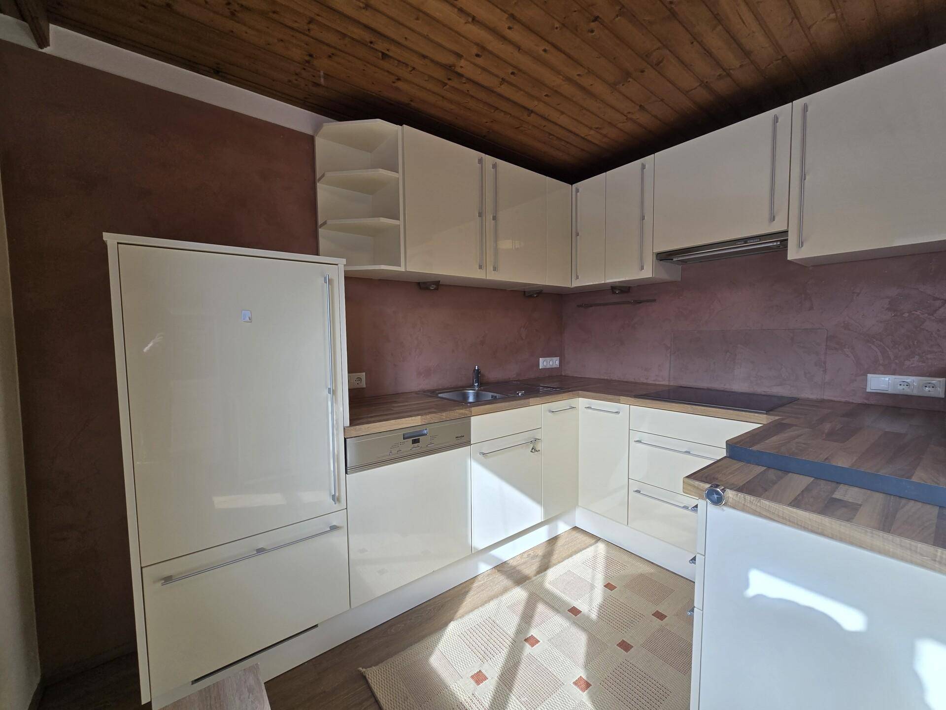 Kompakte Küche mit hellen Schränken, Kühlschrank und Holzarbeitsplatte.