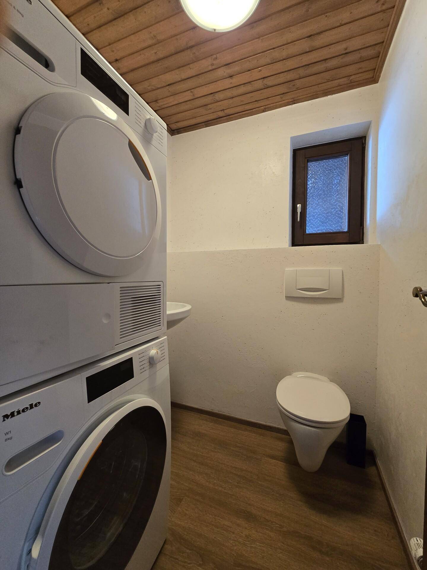 Kleines WC mit Waschmaschine, Trockner und Fenster.